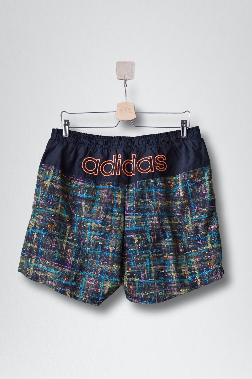 Back view shows a solid black top panel with a large orange ADIDAS logo and the abstract pattern below.