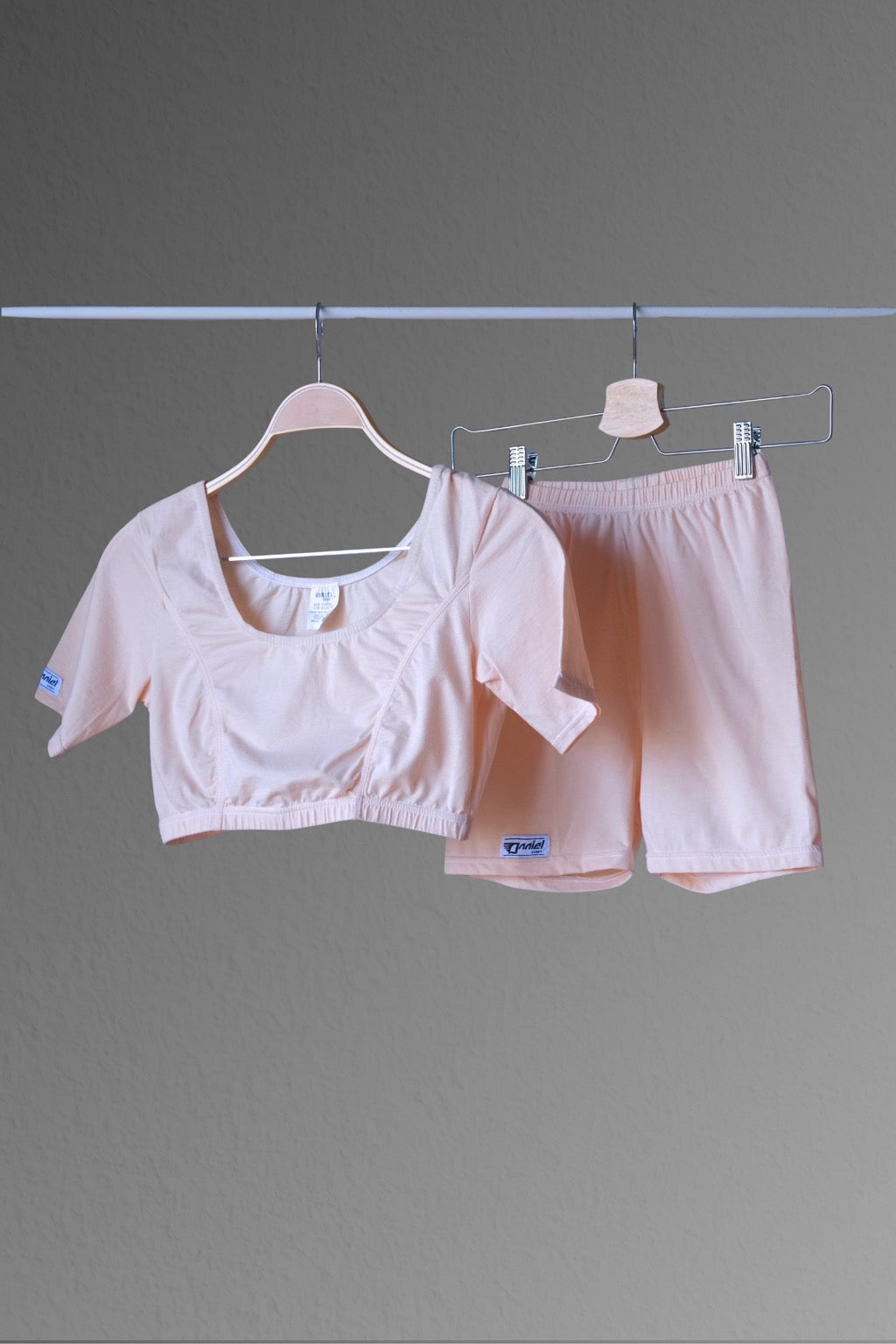 A nude color ANNIEL vintage 90s athletic crop top and shorts set displayed on hangers against a plain grey background. The set includes a cropped top with a wide neckline and matching fitted shorts.
