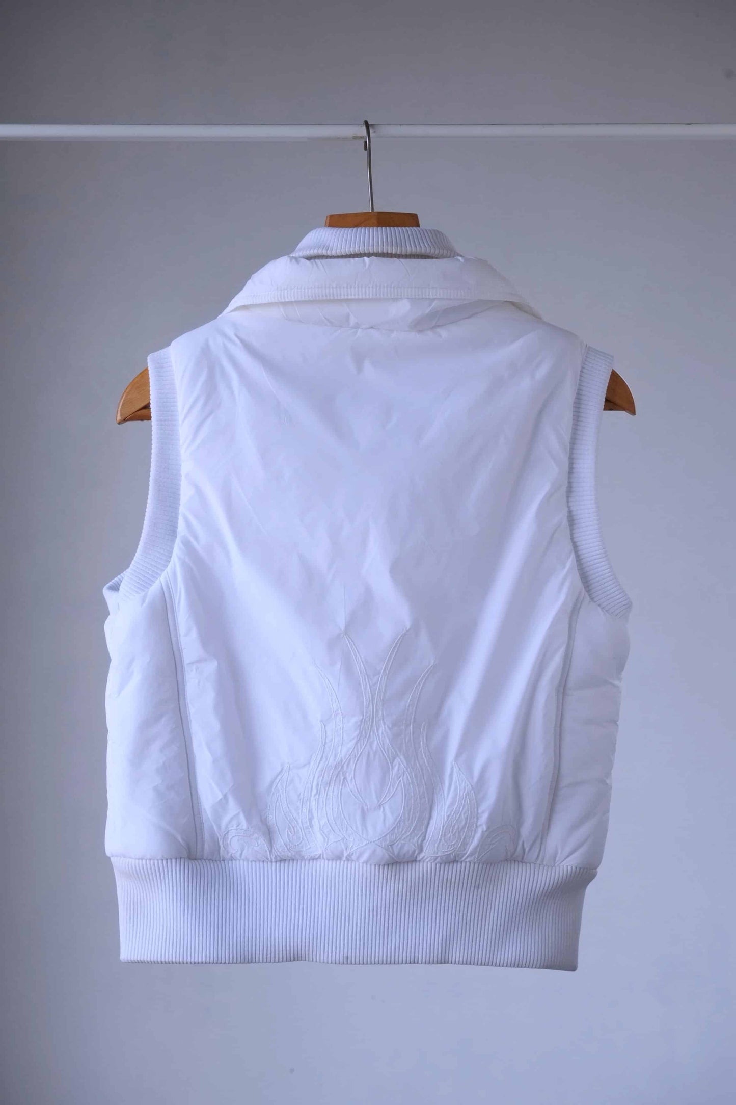 Back view of a white Y2K-style puffer vest featuring intricate embroidered flame detailing with crystal embellishments. The ribbed hem and collar add a structured yet stylish touch.