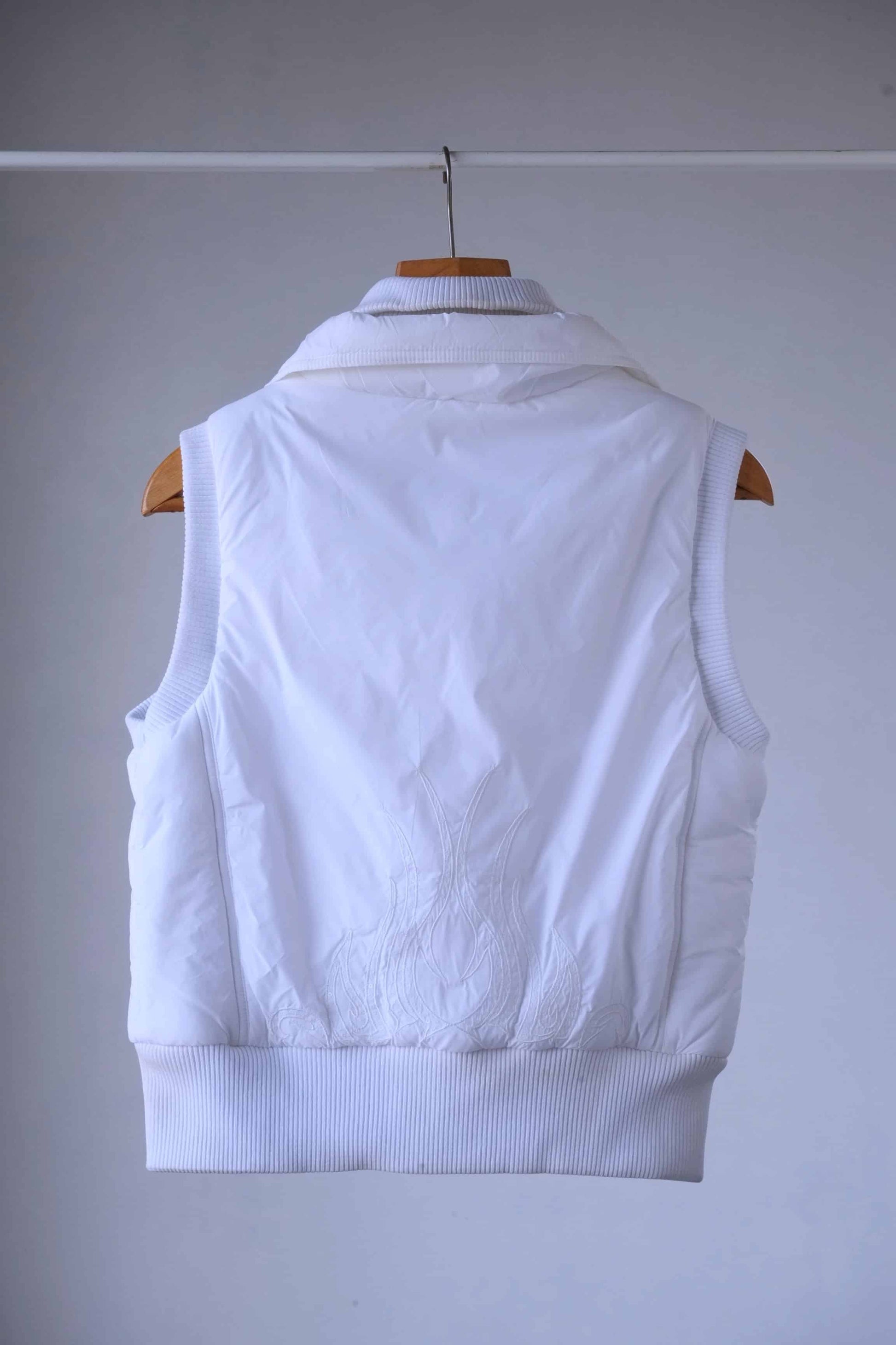 Back view of a white Y2K-style puffer vest featuring intricate embroidered flame detailing with crystal embellishments. The ribbed hem and collar add a structured yet stylish touch.