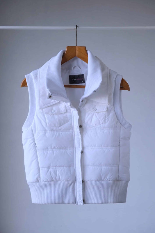 A short, sleeveless Y2K white puffer vest. It has a high collar and a zipper closure. The vest is hanging on a wooden hanger against a light gray background.