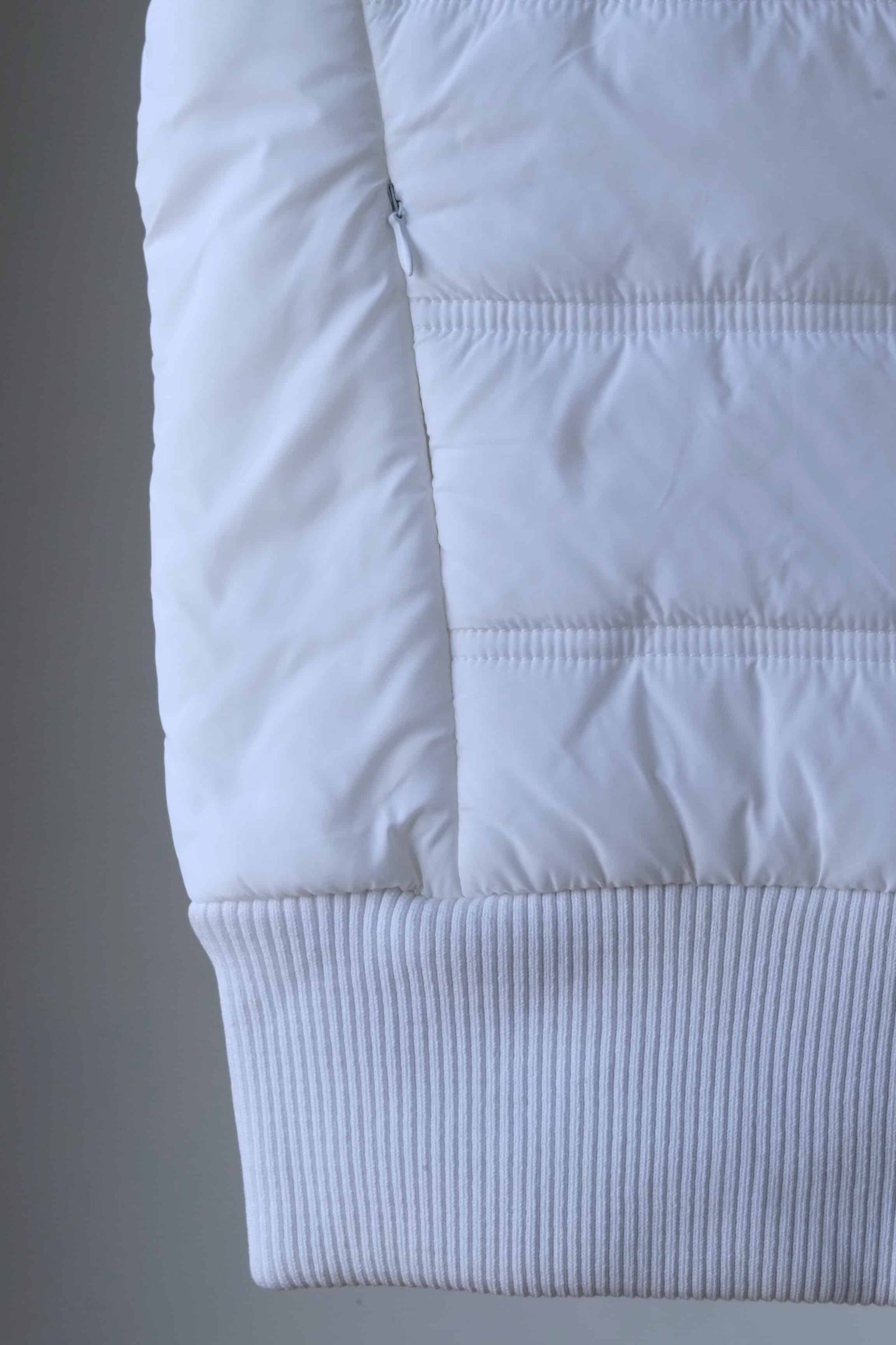 Detail shot of a white sleeveless puffer vest, showcasing the quilted pattern and ribbed hem.