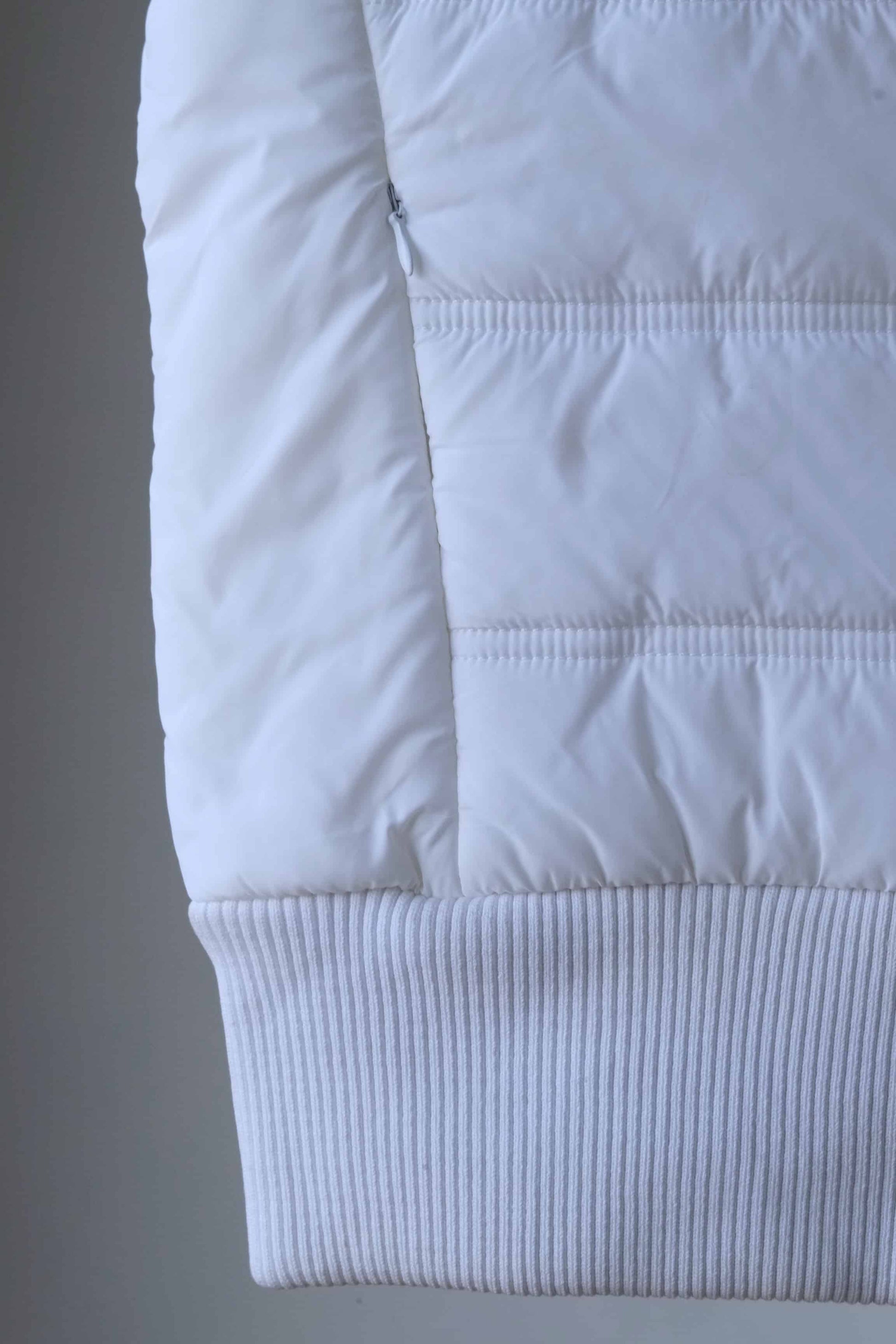 Detail shot of a white sleeveless puffer vest, showcasing the quilted pattern and ribbed hem.