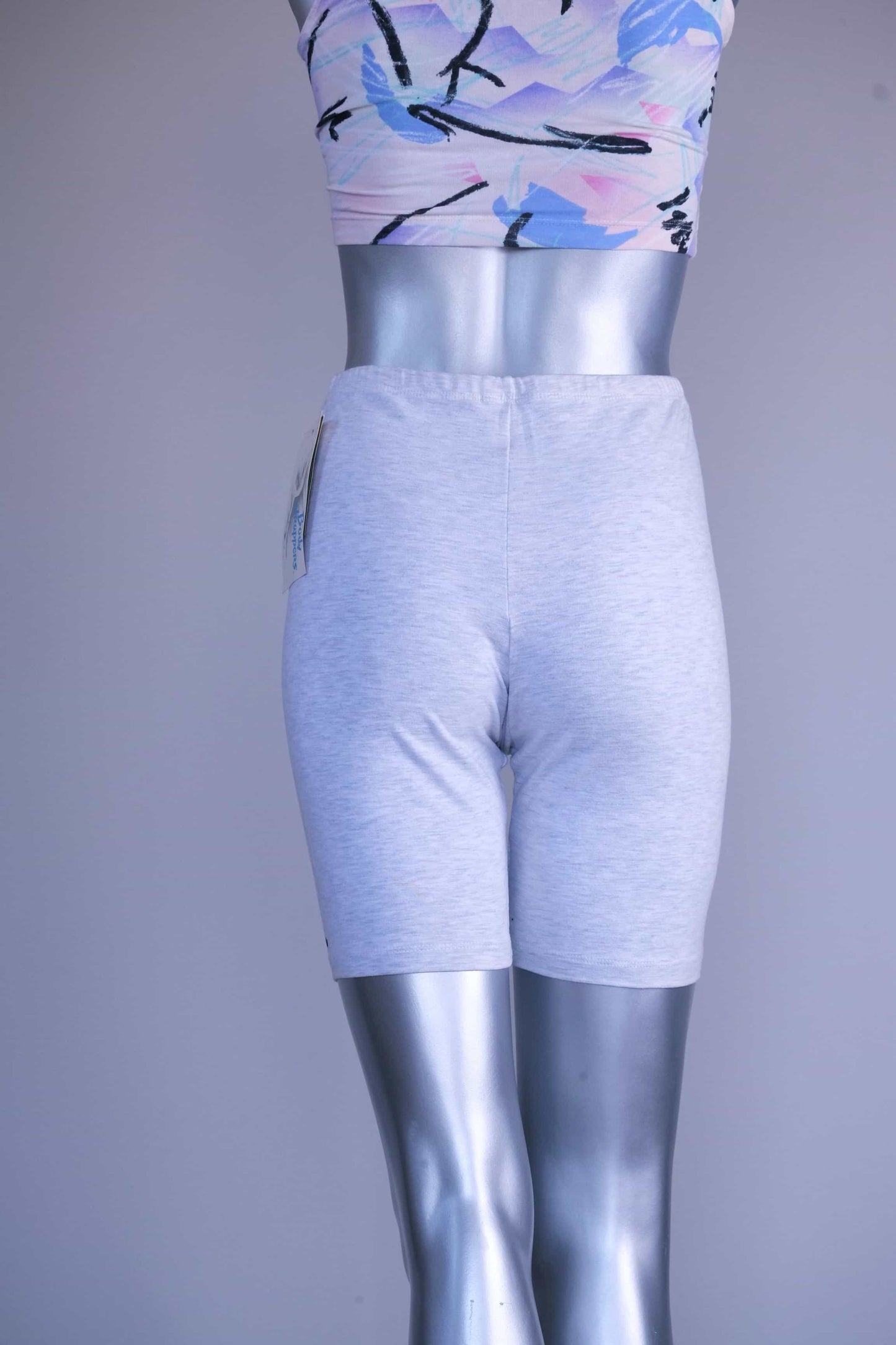 Back view of a mannequin wearing light ash gray vintage 90s BODY WRAPPERS bike shorts and a pastel print crop top.