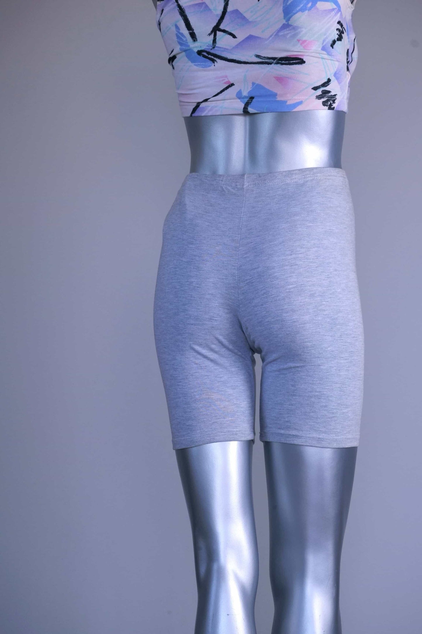 Back view of a mannequin wearing a slightly darker heather gray vintage 90s BODY WRAPPERS bike shorts and a pastel print crop top.
