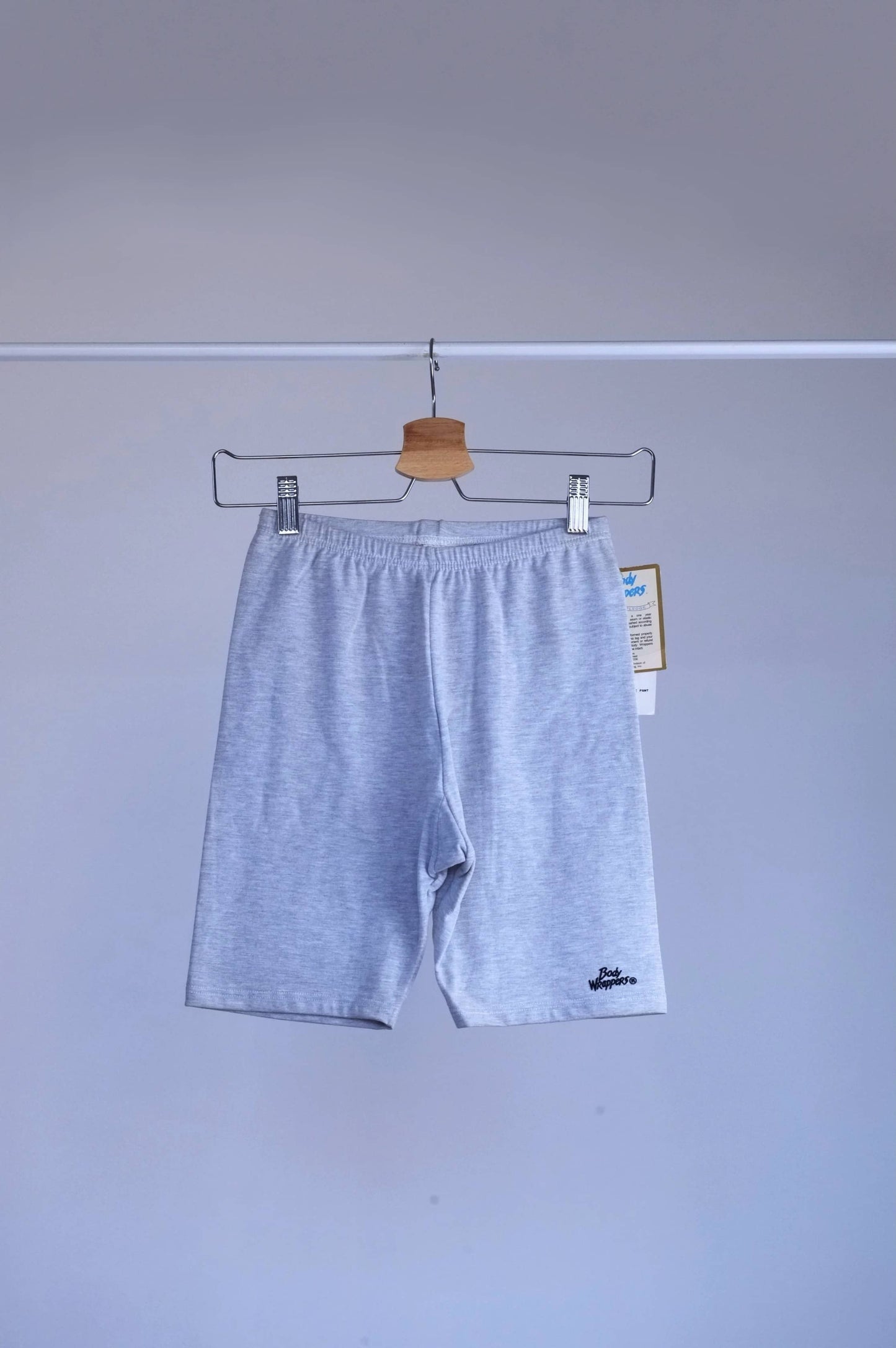 heather grey vintage 90s BODY WRAPPERS bike shorts on a hanger against a gray background.