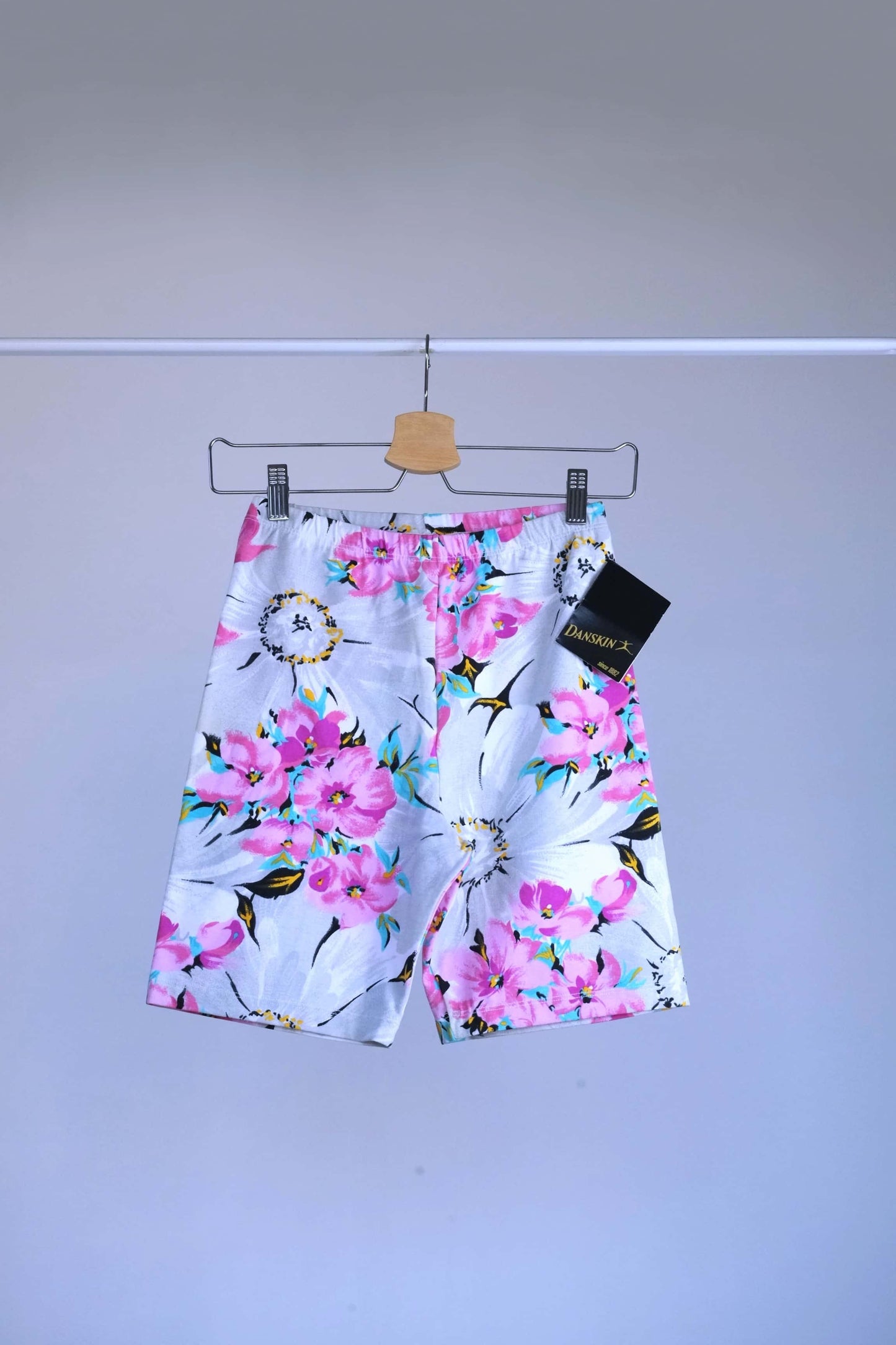 A vintage 90s Danskin activewear biker shorts with a floral print, hanging on a metal rack.