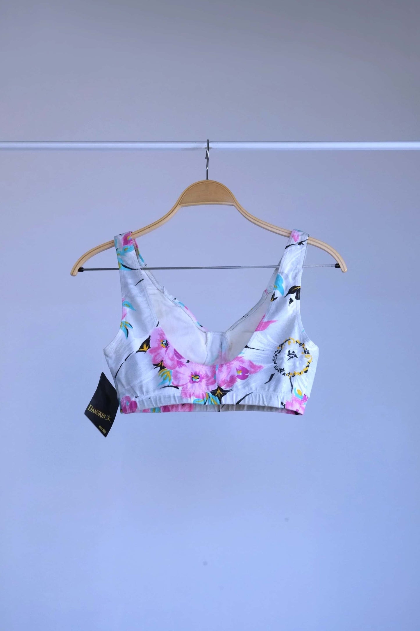 Back view of A vintage 90s Danskin activewear bralette-style crop top with a floral print, hanging on a metal rack.