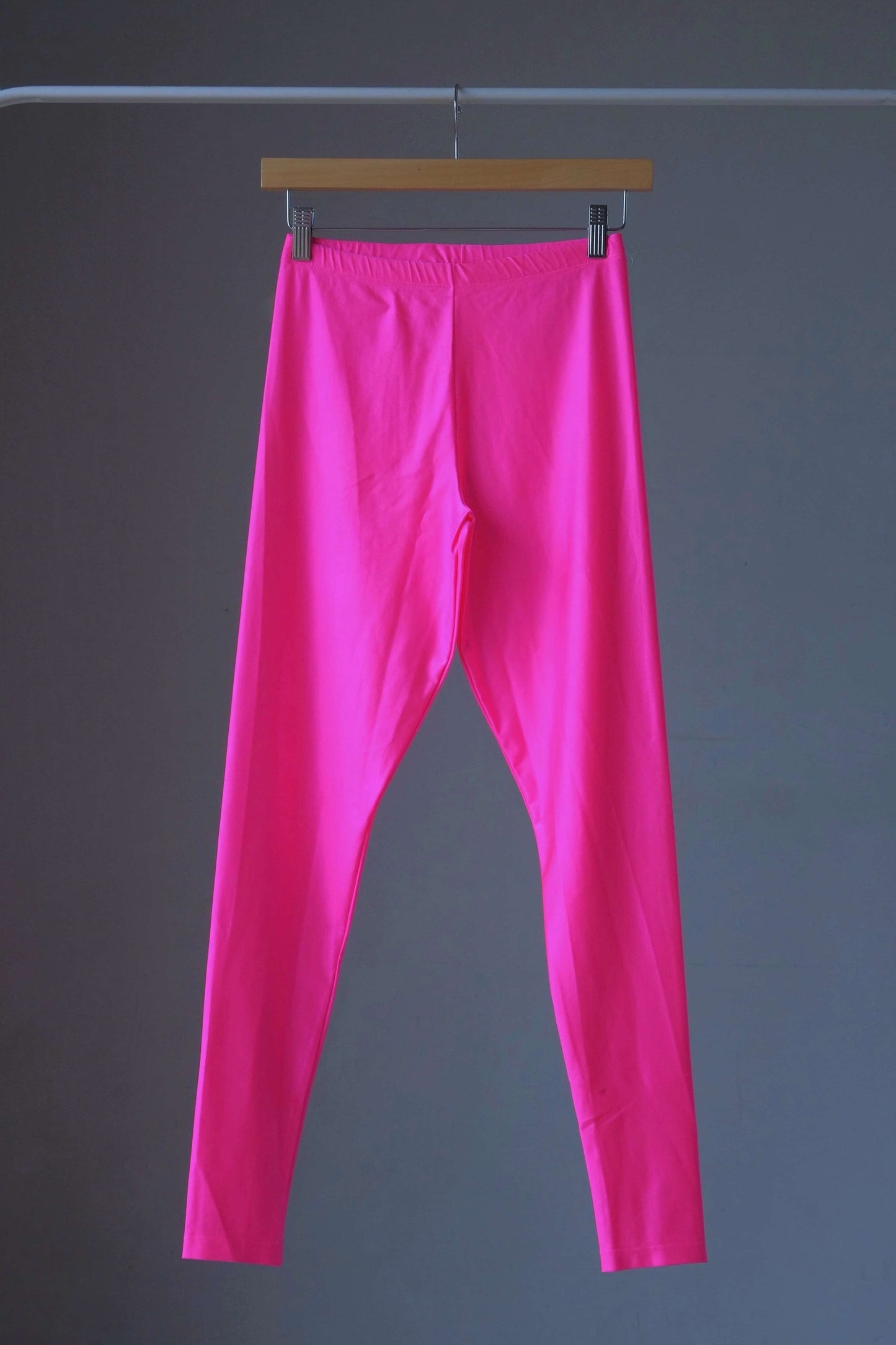 A pair of shiny neon pink vintage 90s Danskin high-waist leggings displayed on a hanger.