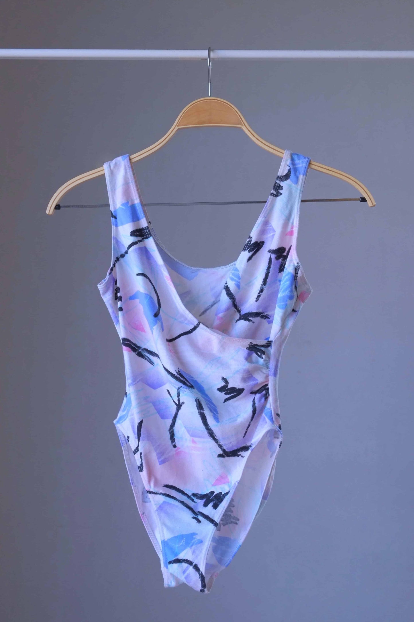 Front view of a vintage Danskin leotard with a pastel abstract print on a hanger.