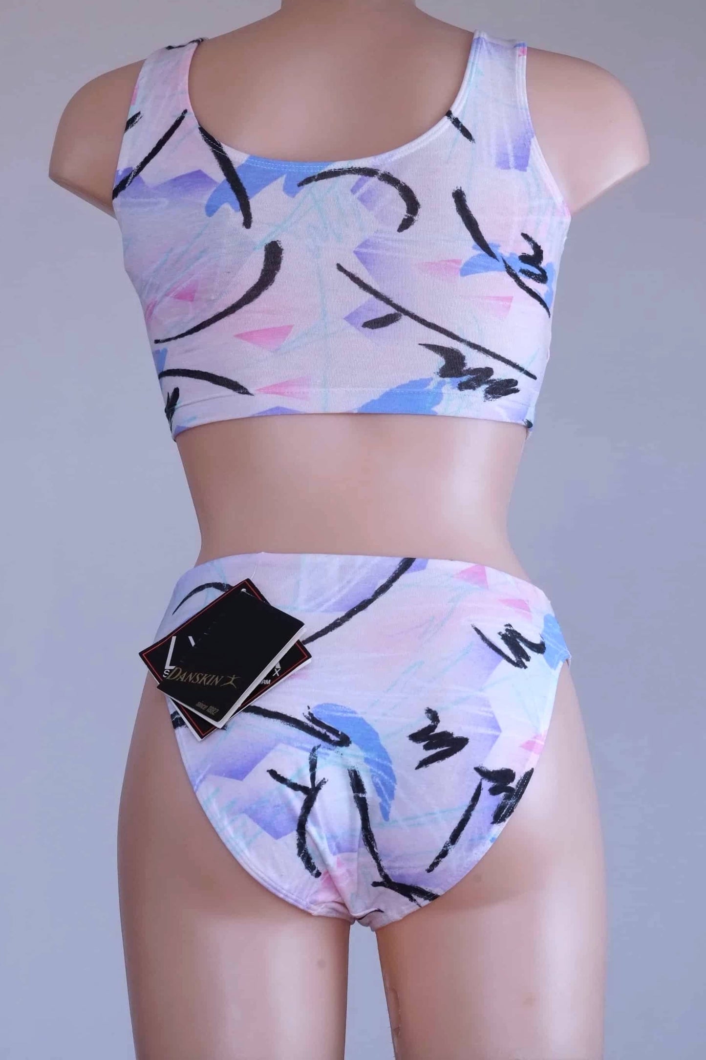 Back view of a DANSKIN vintage 90s matching activewear set, featuring a pastel abstract print crop top and high-cut briefs, displayed on a mannequin.