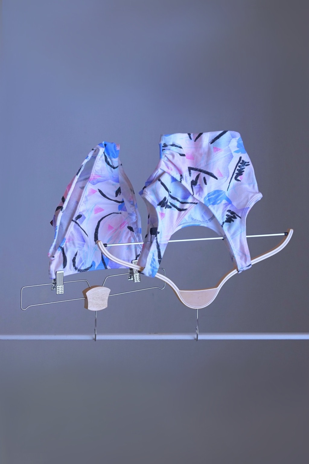 A DANSKIN vintage 90s matching activewear set, featuring a pastel abstract print crop top and high-cut briefs, displayed on hangers.