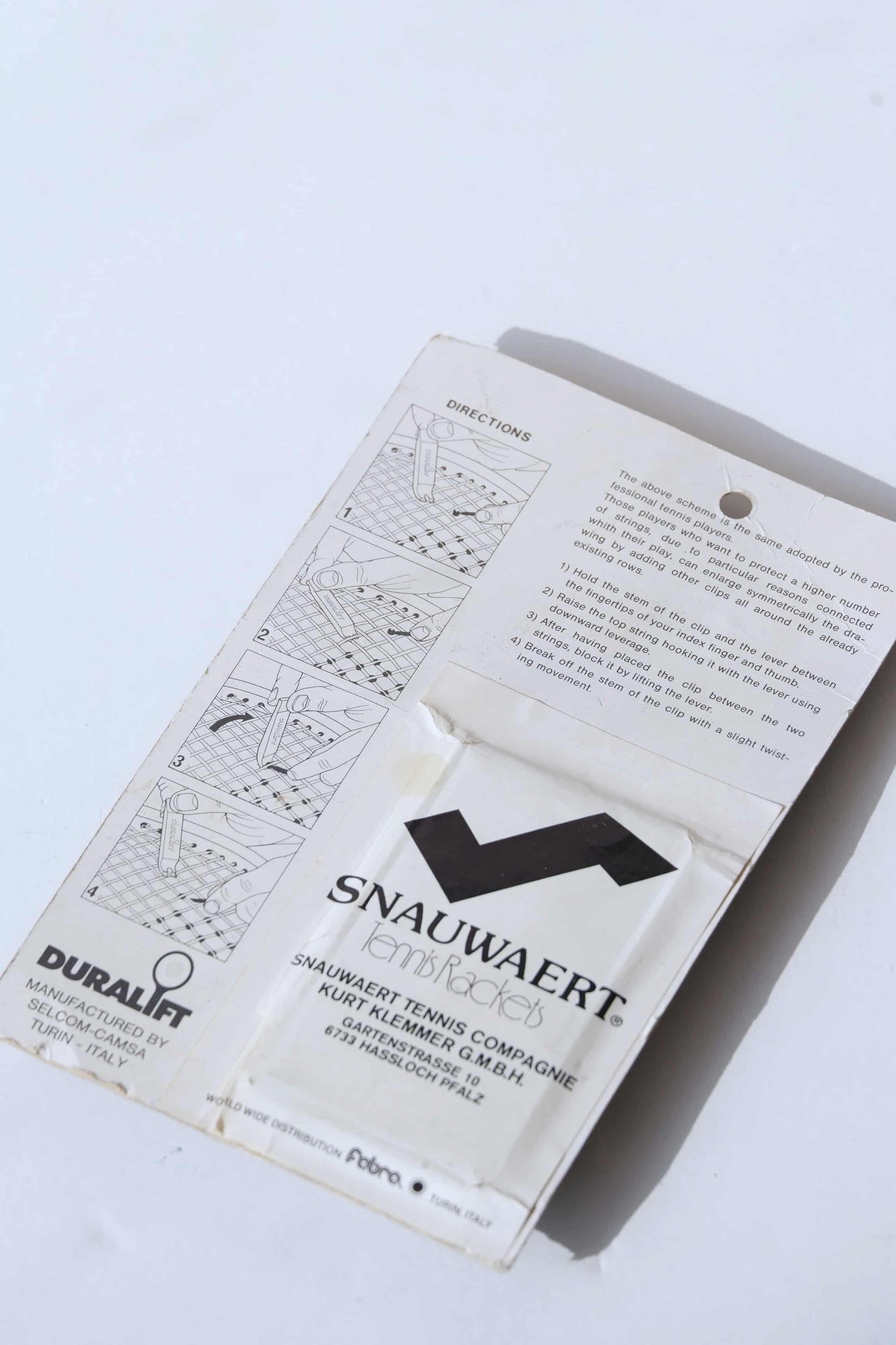 Close up of the Backside of a vintage Duralift Micrograph Tennis String Saver Kit. It is white with black text. The word SNAUWAERT is visible with a stylized S which looks like the logo of the brand.