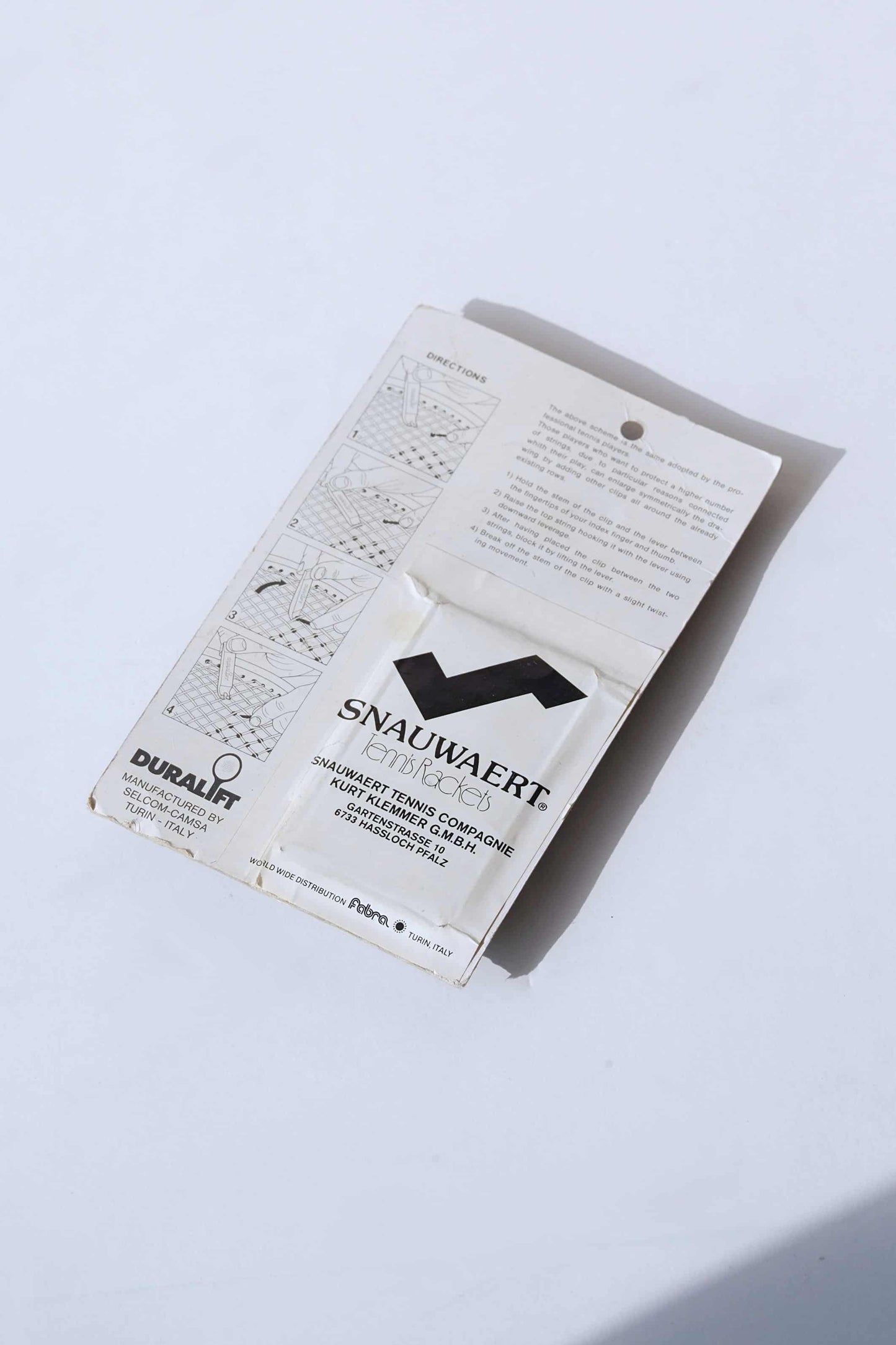 Backside of a vintage Duralift Micrograph Tennis String Saver Kit. It is white with black text. The word SNAUWAERT is visible with a stylized S which looks like the logo of the brand.