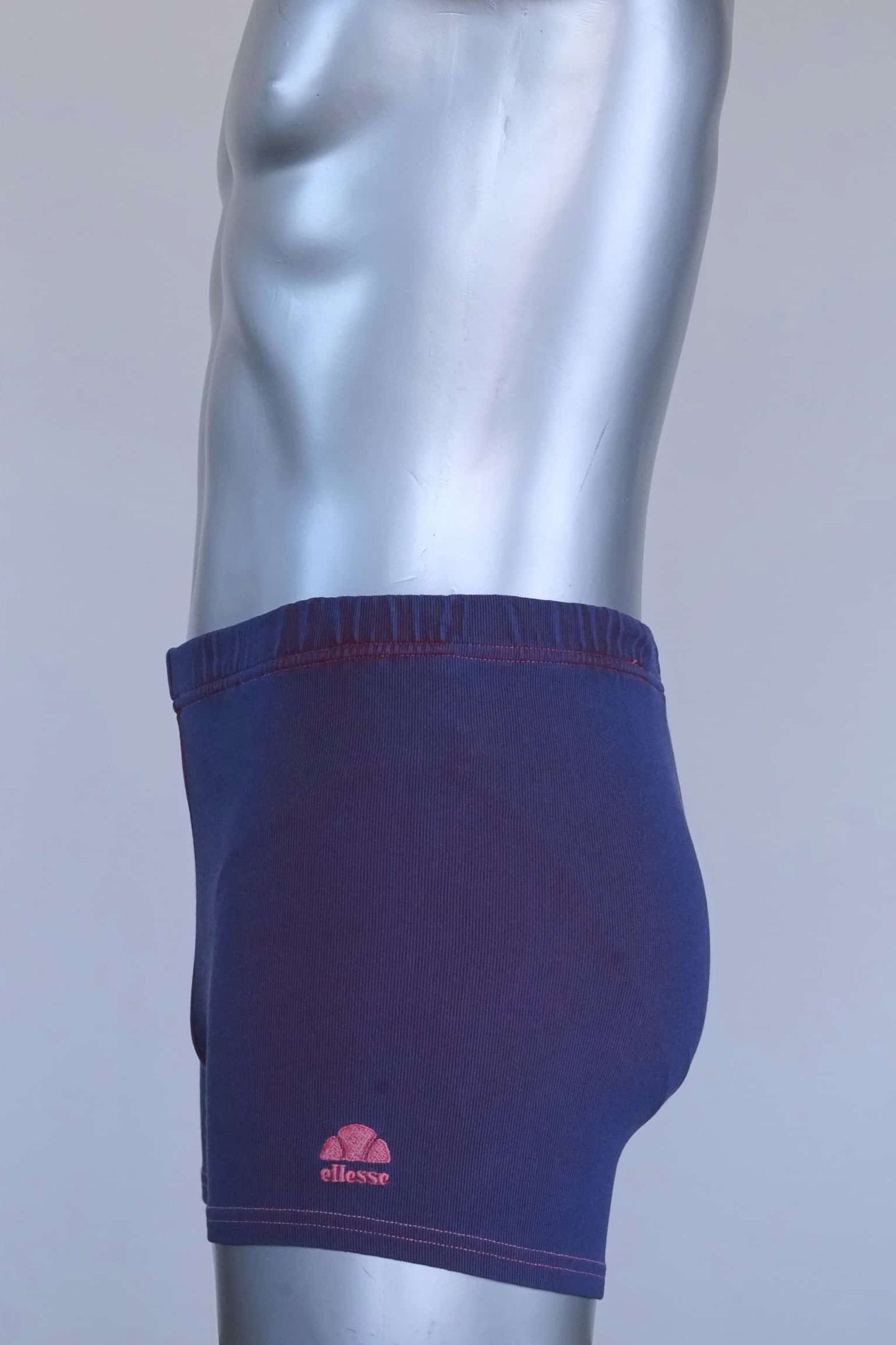 Side profile of vintage 90s Ellesse men’s swim trunks with embroidered pink logo at hem.
