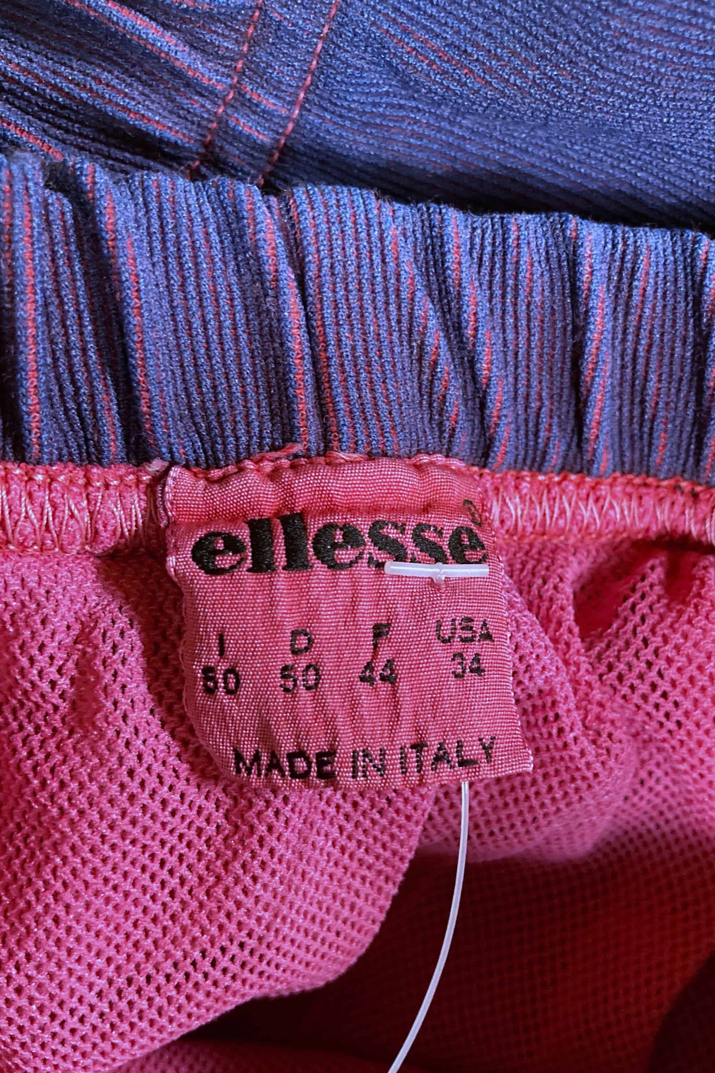 Close-up of pink Ellesse size tag reading 50 Italy, 34 USA, made in Italy.