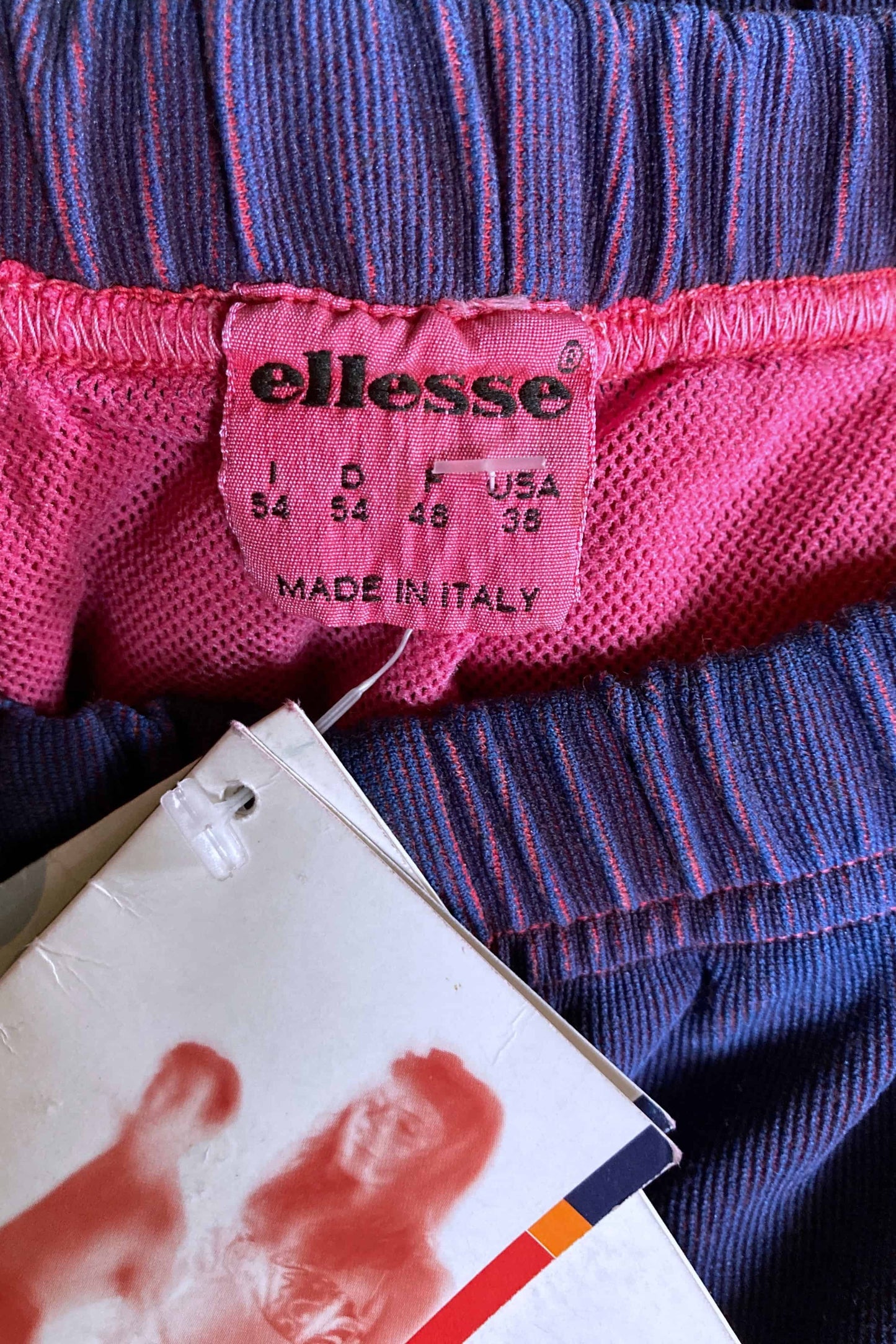 Close-up of pink Ellesse size tag reading 54 Italy, 38 USA, made in Italy.