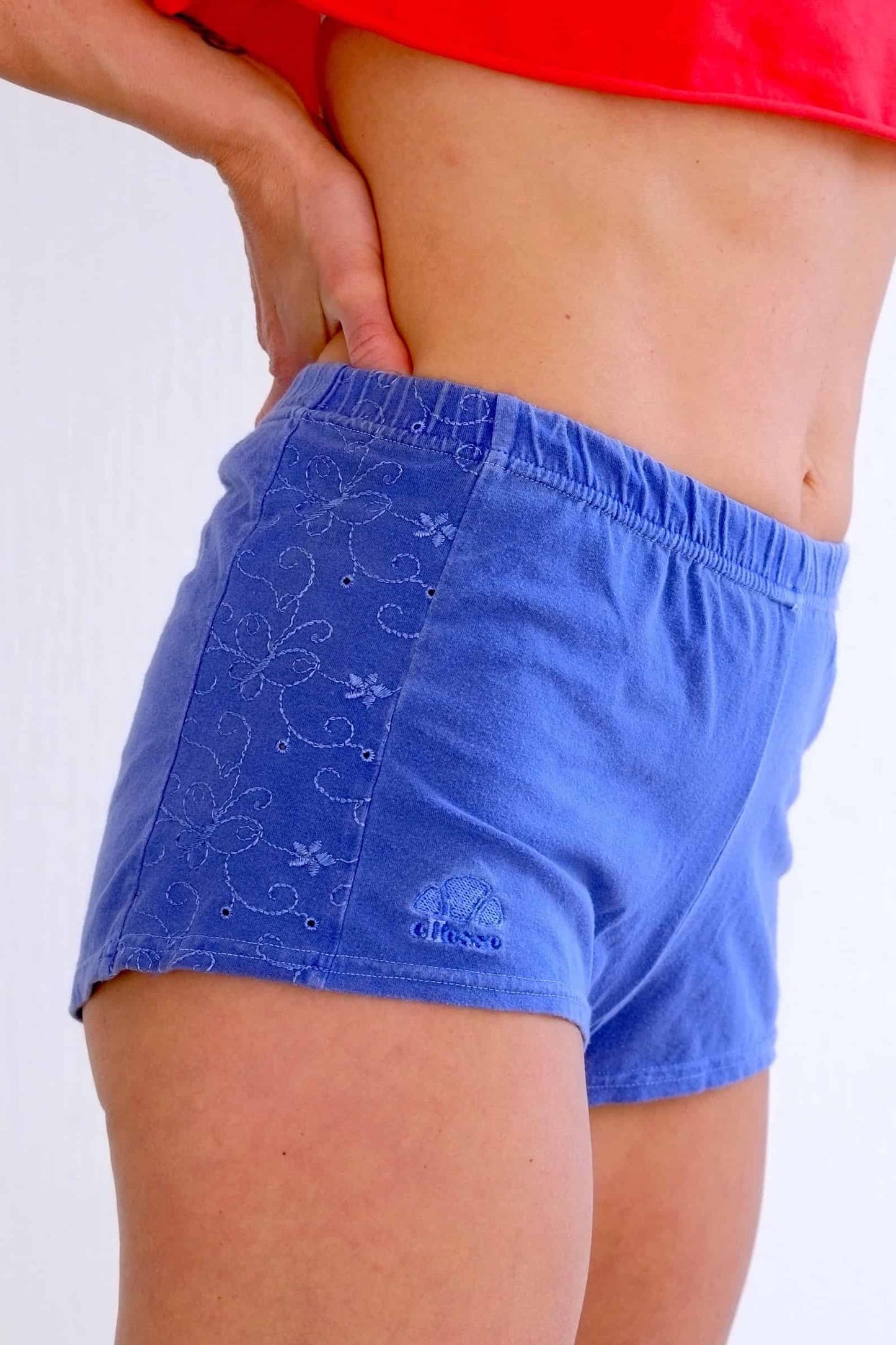 Close-up of vintage Ellesse blue terry hot pants with floral embroidery and logo.