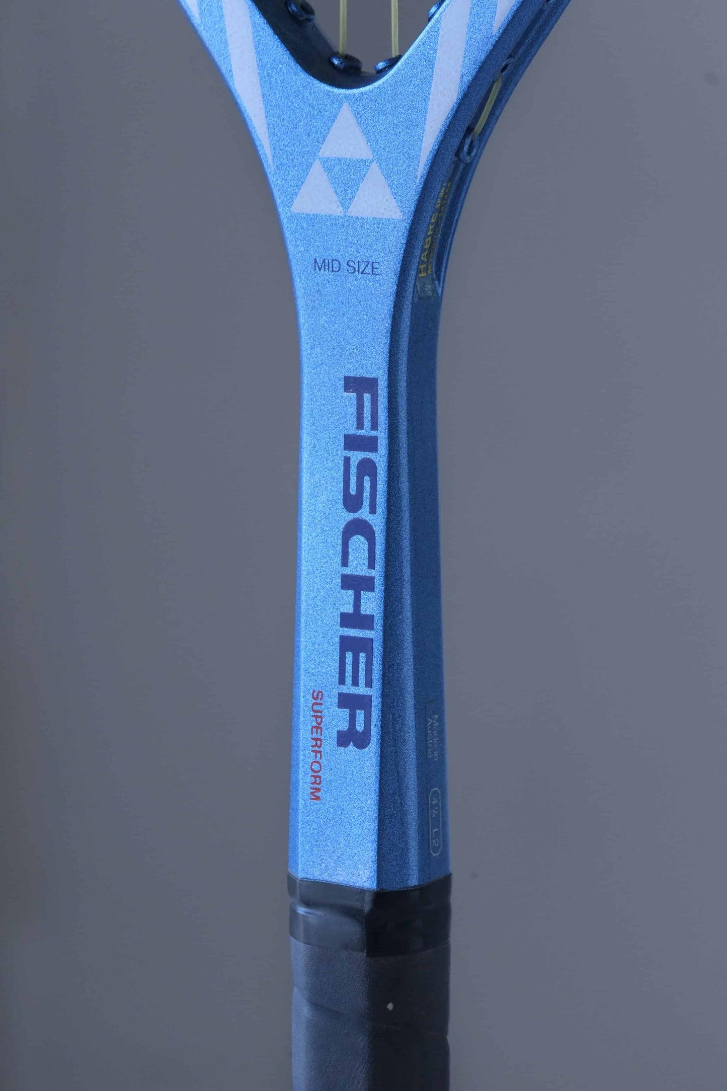 Close-up of a tennis racket neck with a blue and black handle.
The word "FISCHER" is written in navy on the handle, with "SUPERFORM" written below it. The words "MID SIZE" are also visible on the handle, as well as the triangular Fischer logo.