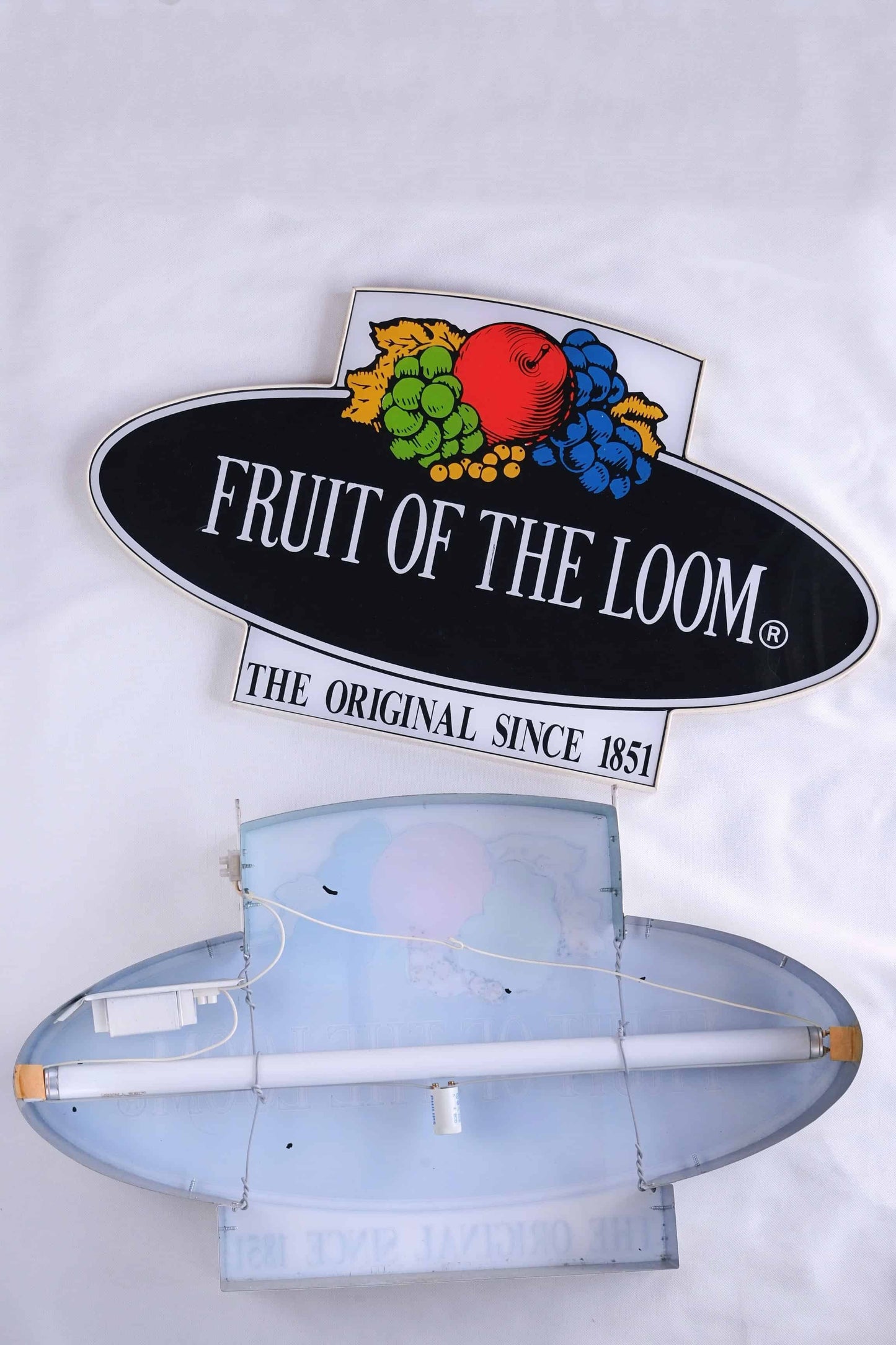 Front view of vintage 1990s Fruit of the Loom light-up store sign showing internal fluorescent tube and wiring, with detached front panel featuring classic logo.