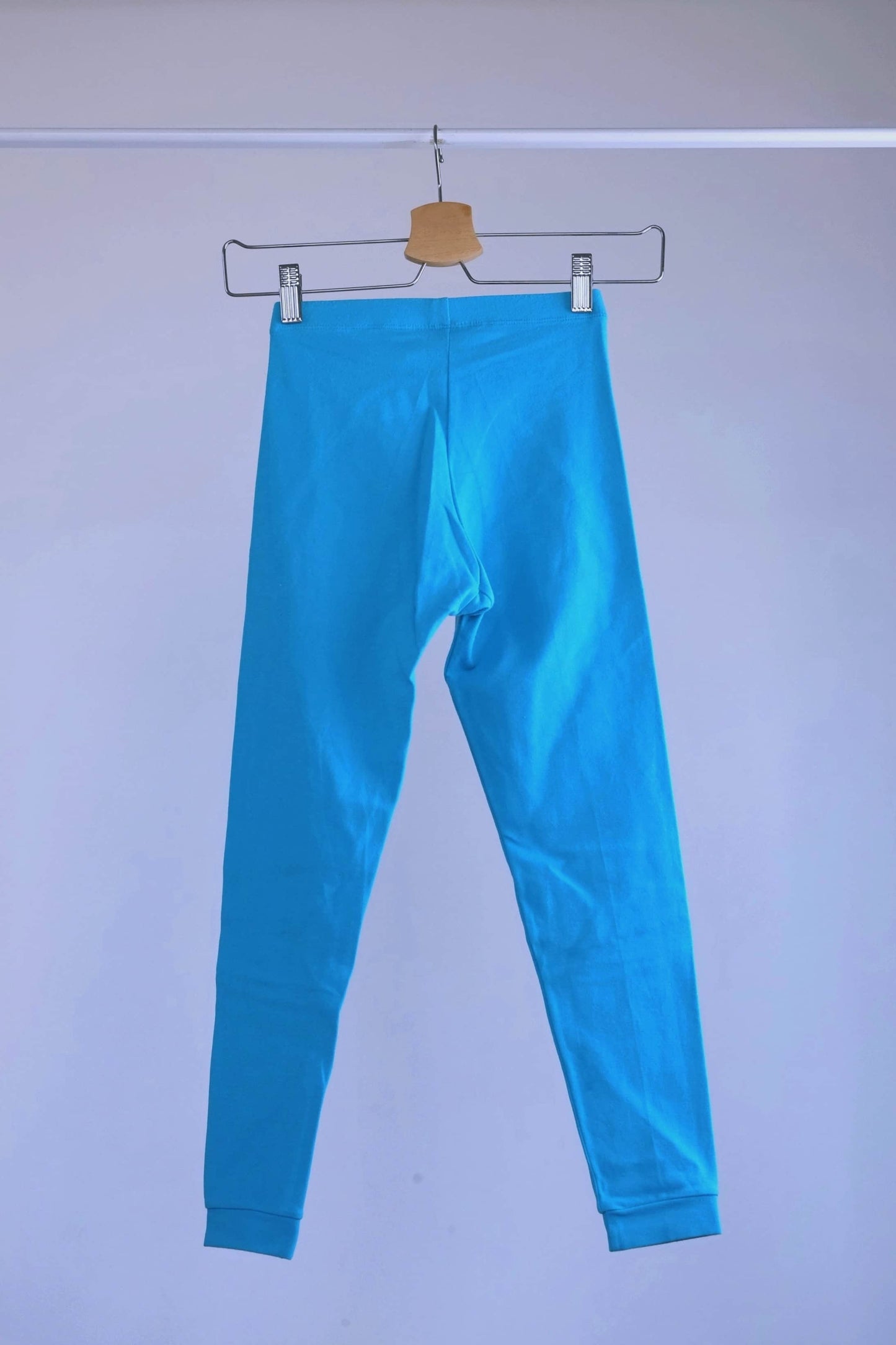 Back view of A pair of blue, vintage 90s GILDA MARX cropped leggings hanging on a metal hanger against a light gray background.