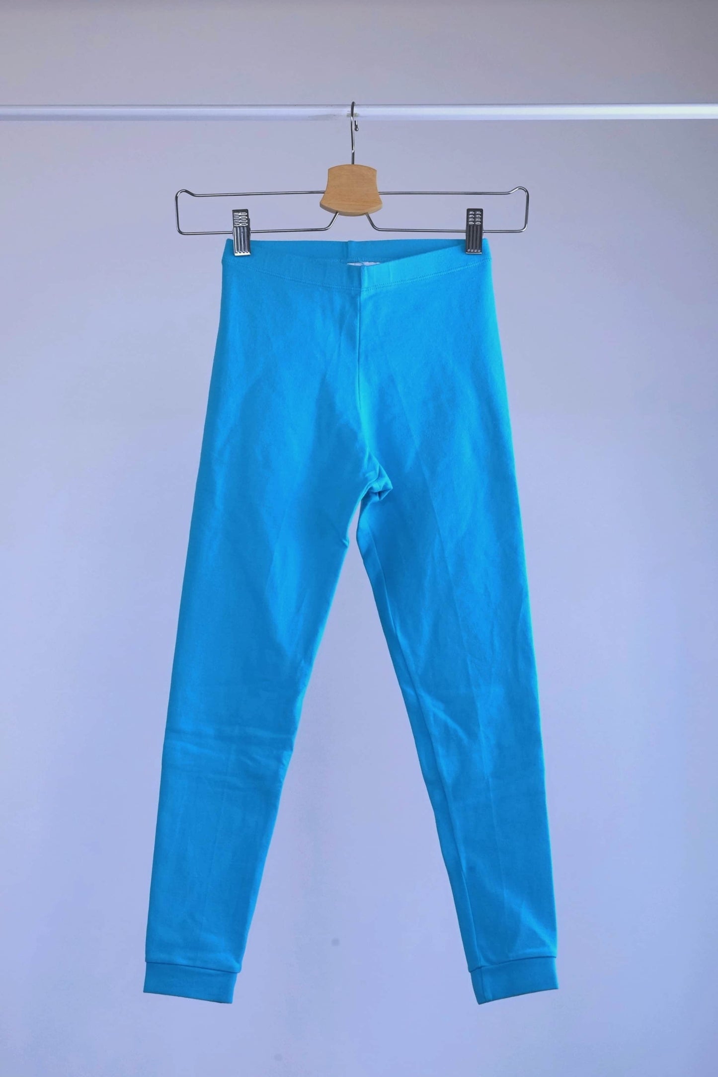 A pair of blue, vintage 90s GILDA MARX cropped leggings hanging on a metal hanger against a light gray background.
