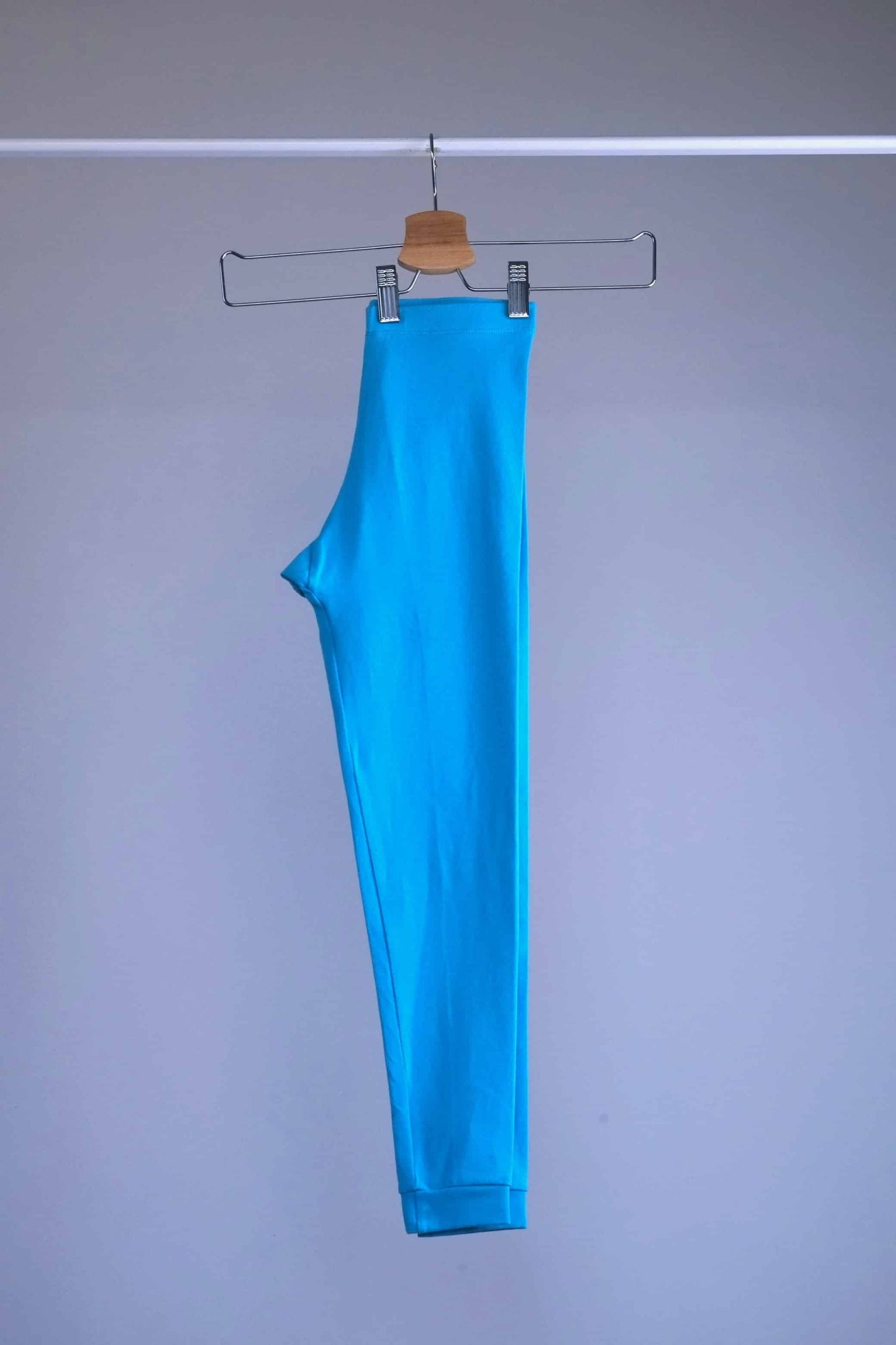 Side view of A pair of blue, vintage 90s GILDA MARX cropped leggings hanging on a metal hanger against a light gray background.