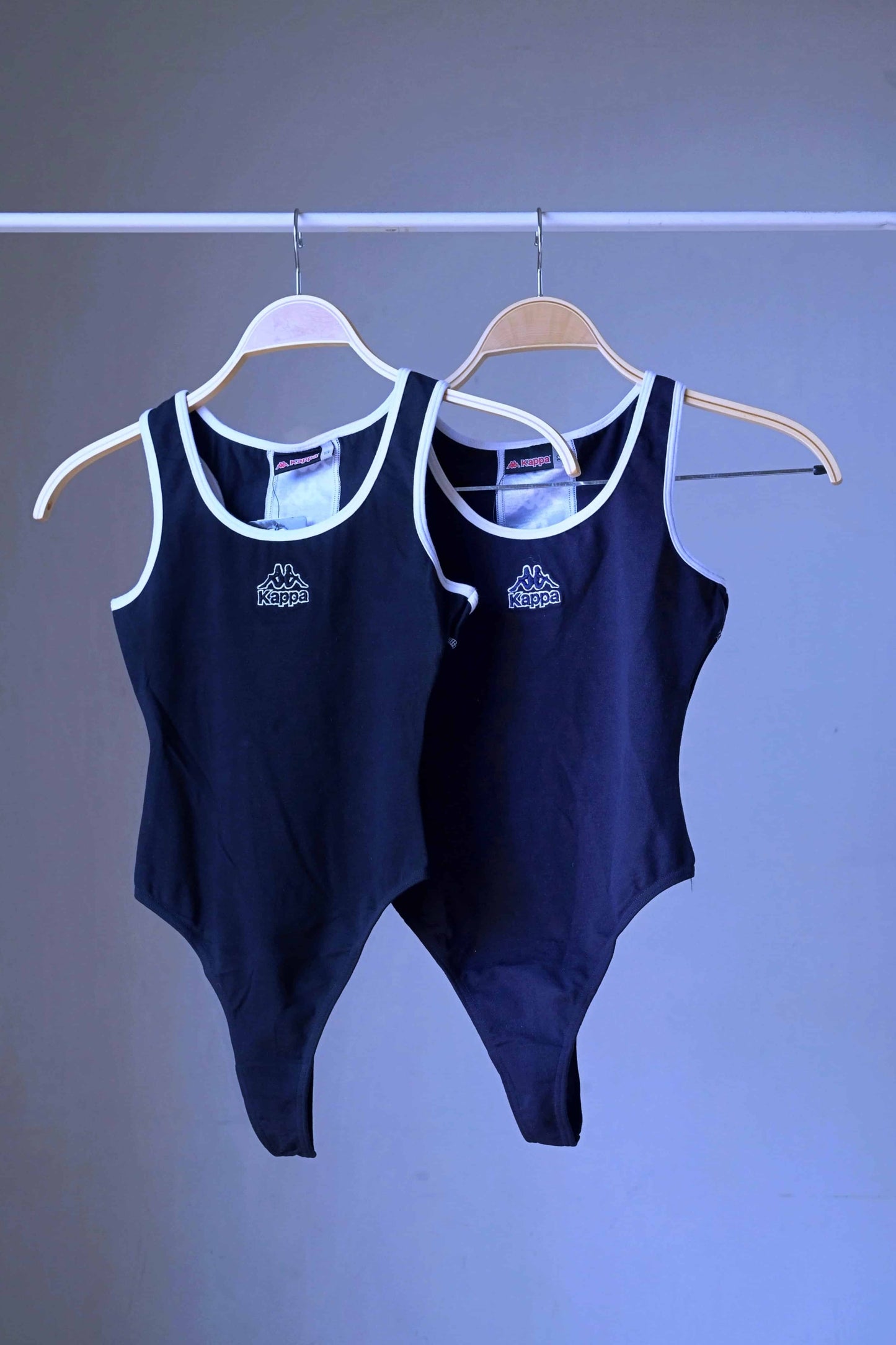 Two black KAPPA vintage 90s women's activewear leotards, one dark navy and one black, with white trim and chest logos, displayed side-by-side on hangers.