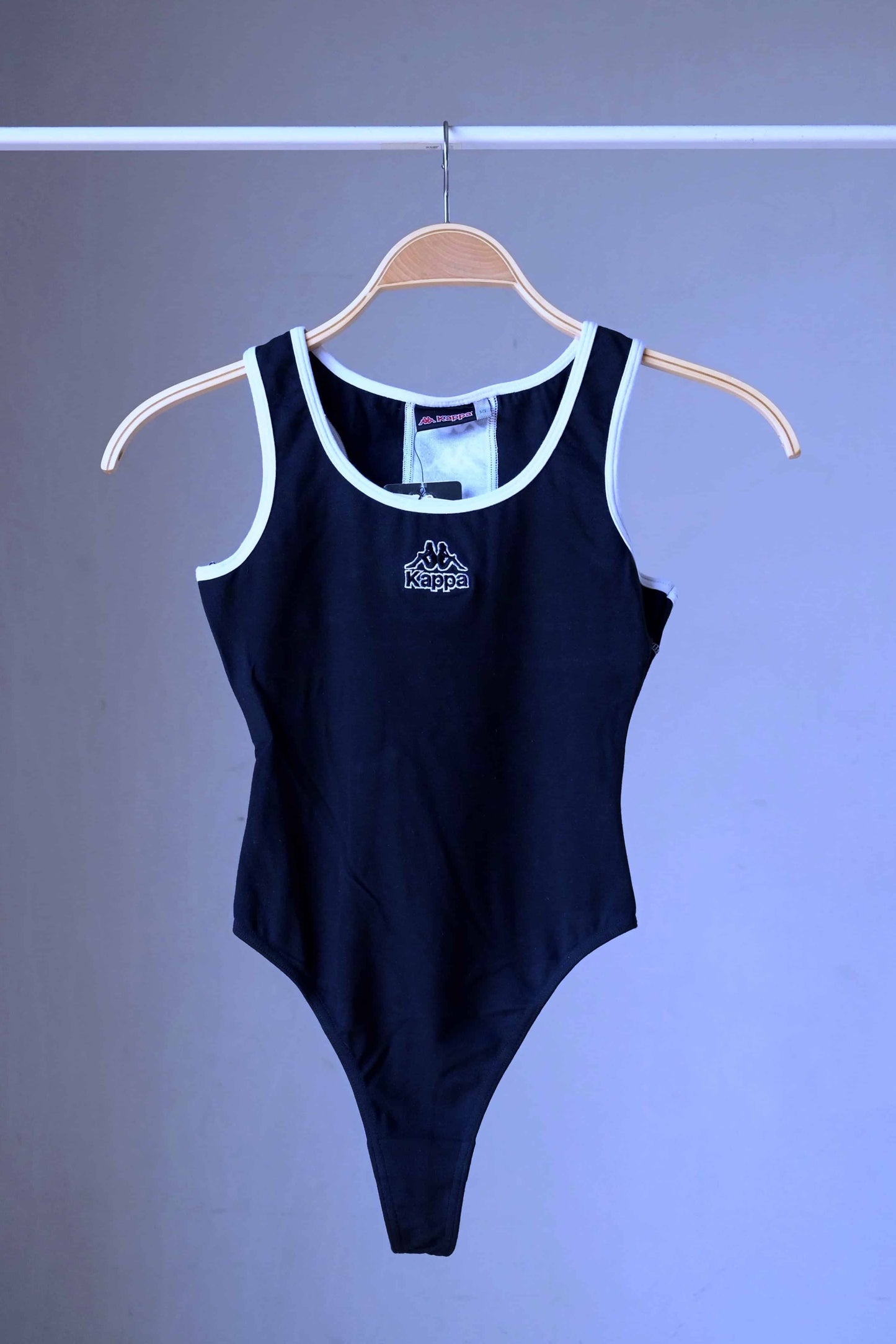 Front view of a black KAPPA vintage 90s women's activewear leotard with white trim and a chest logo, displayed on a wooden hanger.