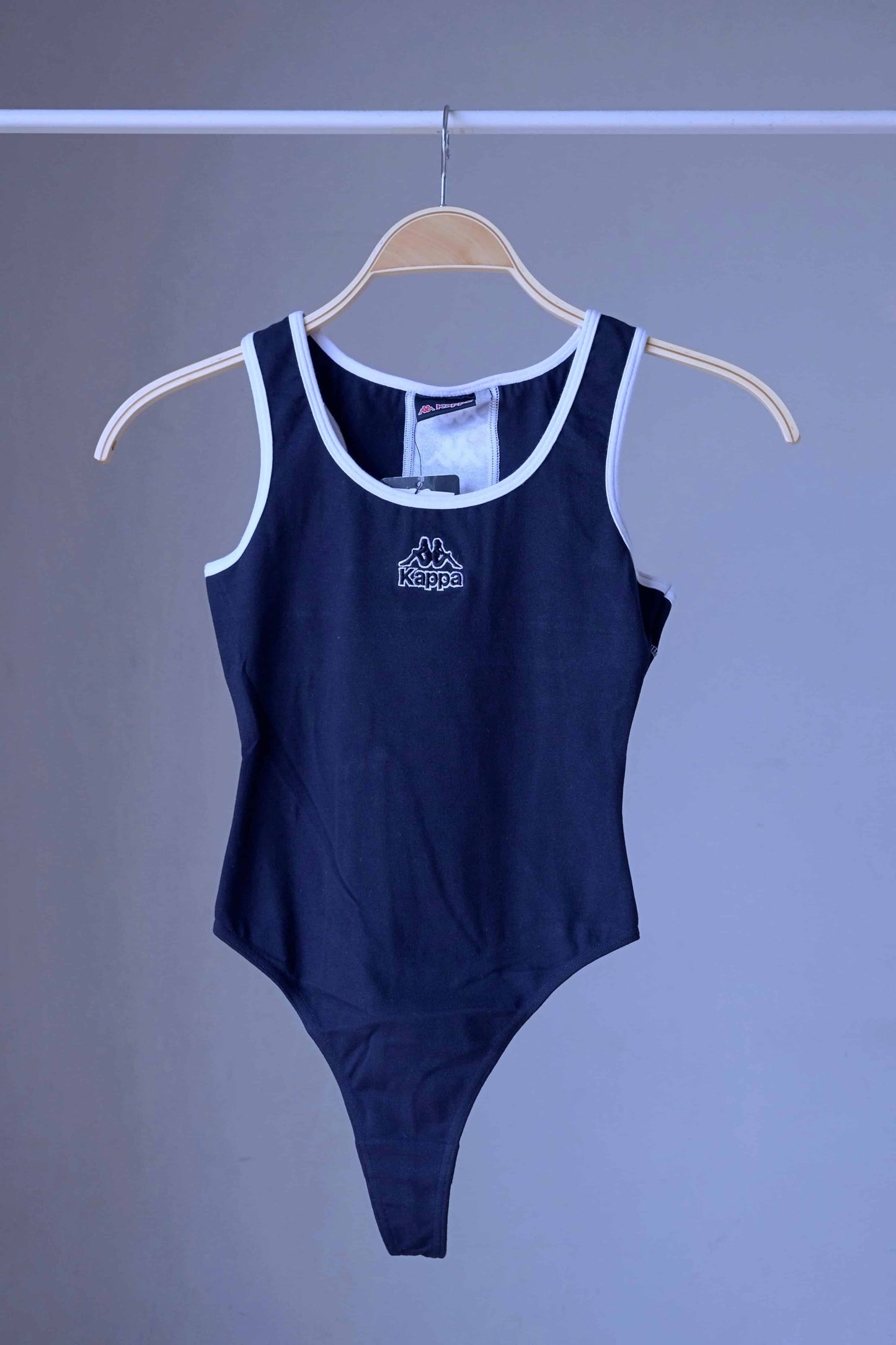 Front view of a navy KAPPA vintage 90s women's activewear leotard with white trim and a chest logo, displayed on a wooden hanger.