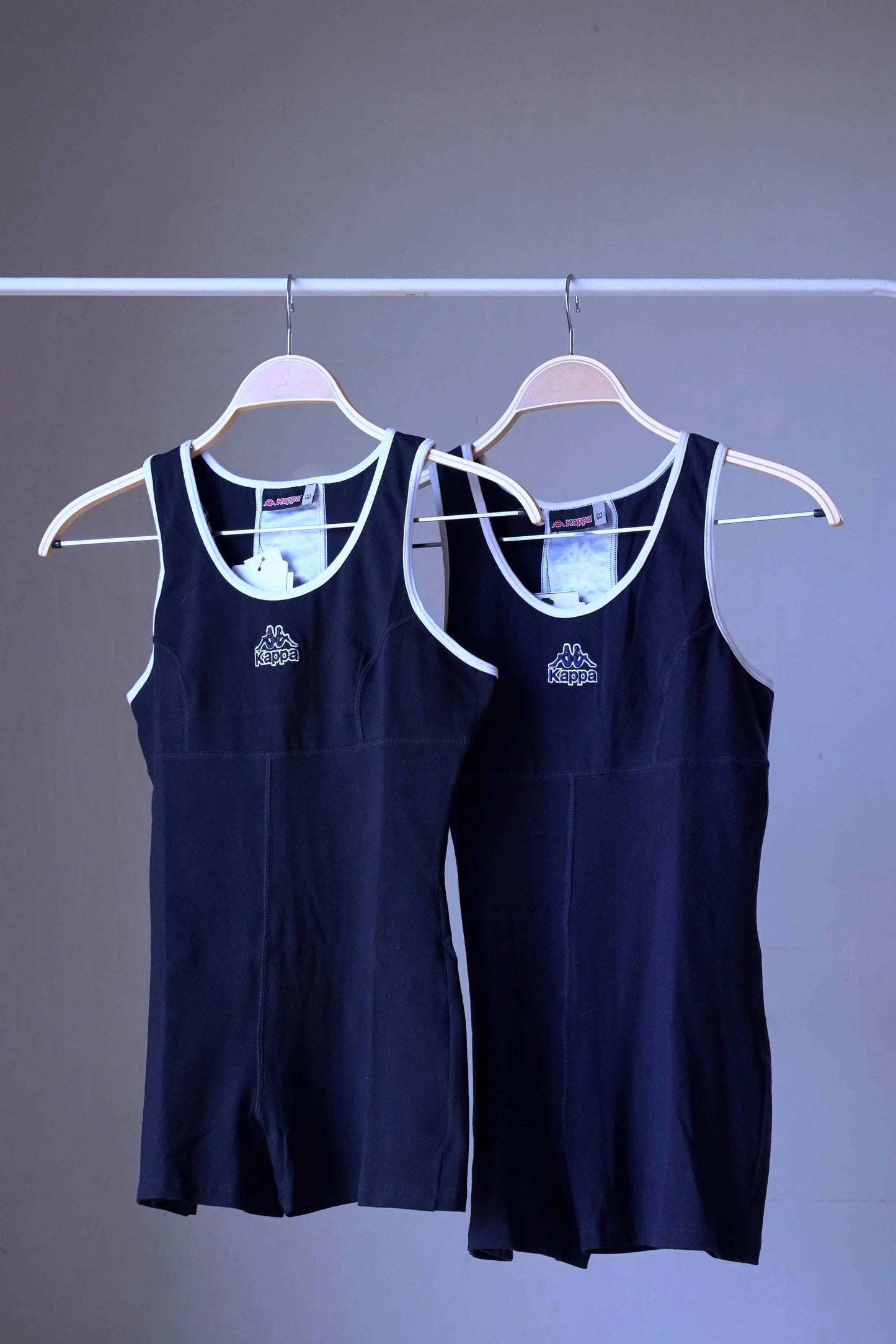 Two KAPPA vintage 90s women's activewear biketards on hangers. One is black and the other is navy, both with white trim and a KAPPA logo on the chest.