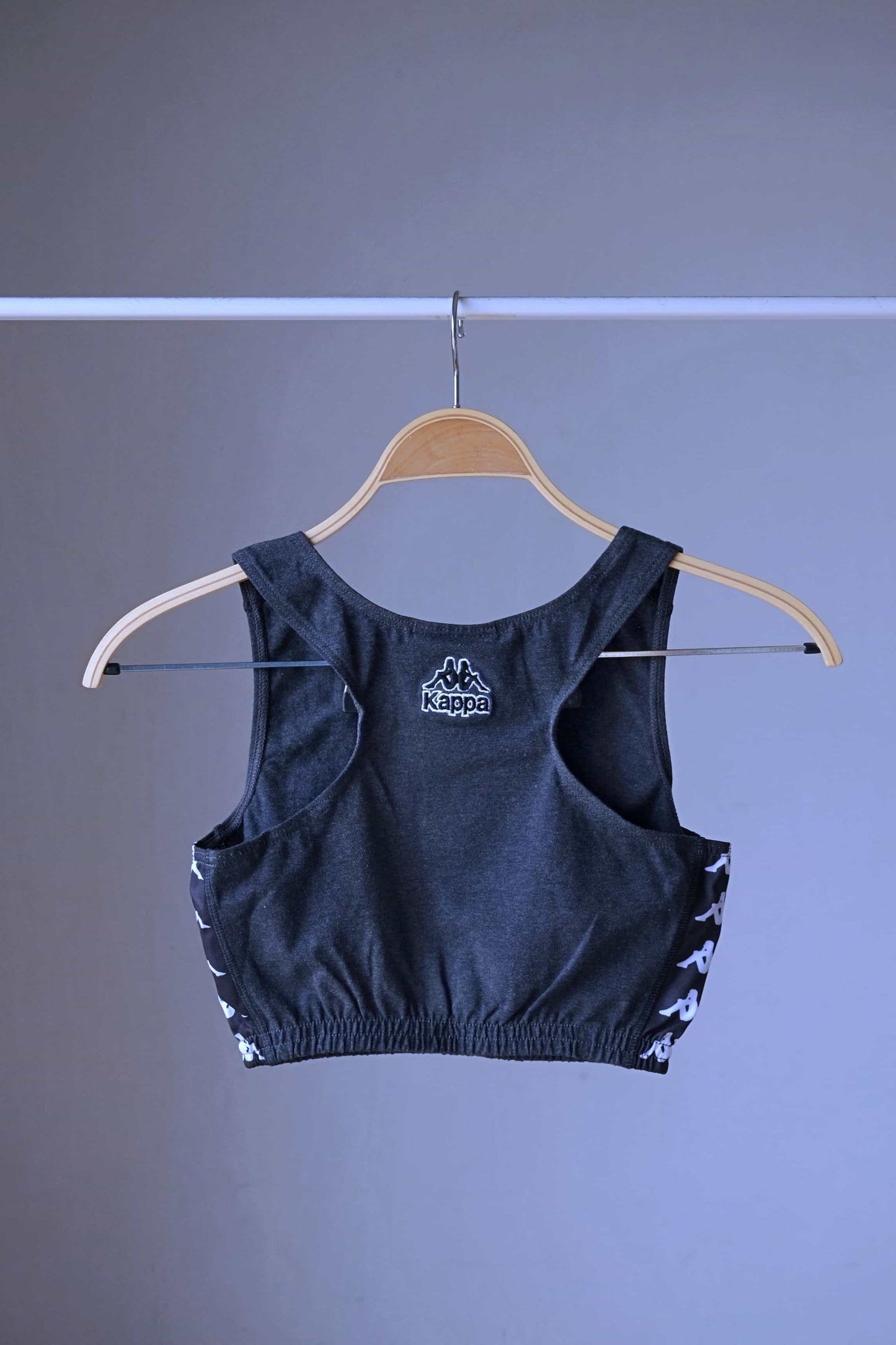 Back view of a charcoal grey KAPPA vintage women's athletic crop top on a wooden hanger, showing the white KAPPA logo on the back and white logo taping along the sides.