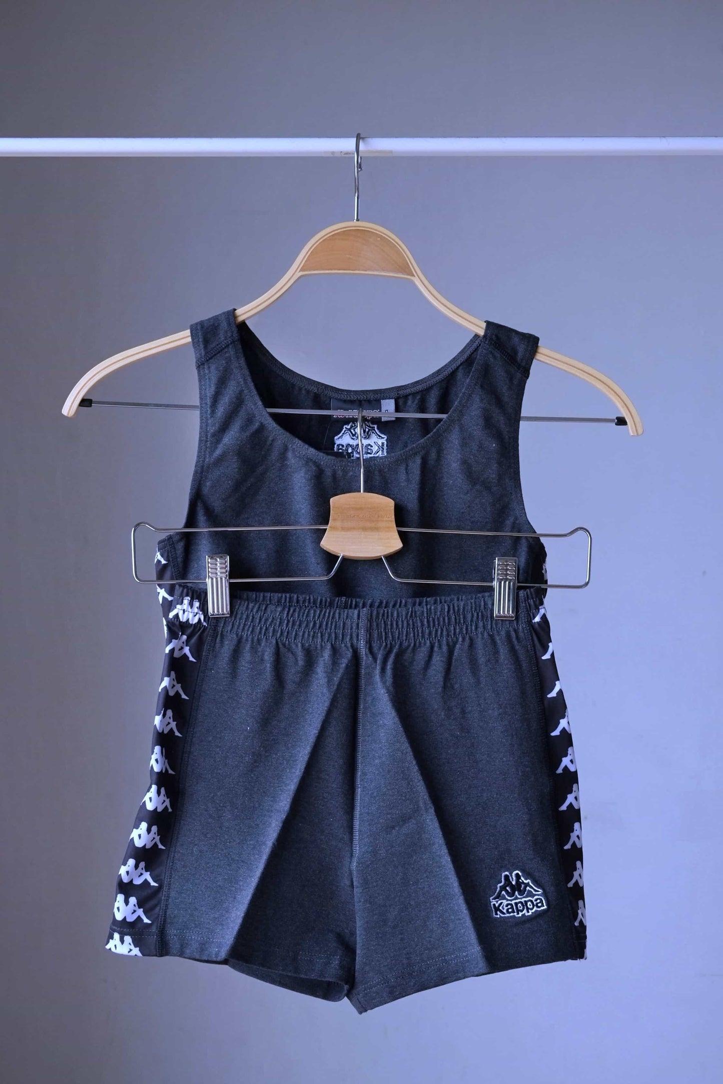 Front view of a charcoal grey KAPPA vintage women's athletic crop top and shorts set on a hanger, with the shorts hanging below the top, displaying the white logo taping on both garments.
