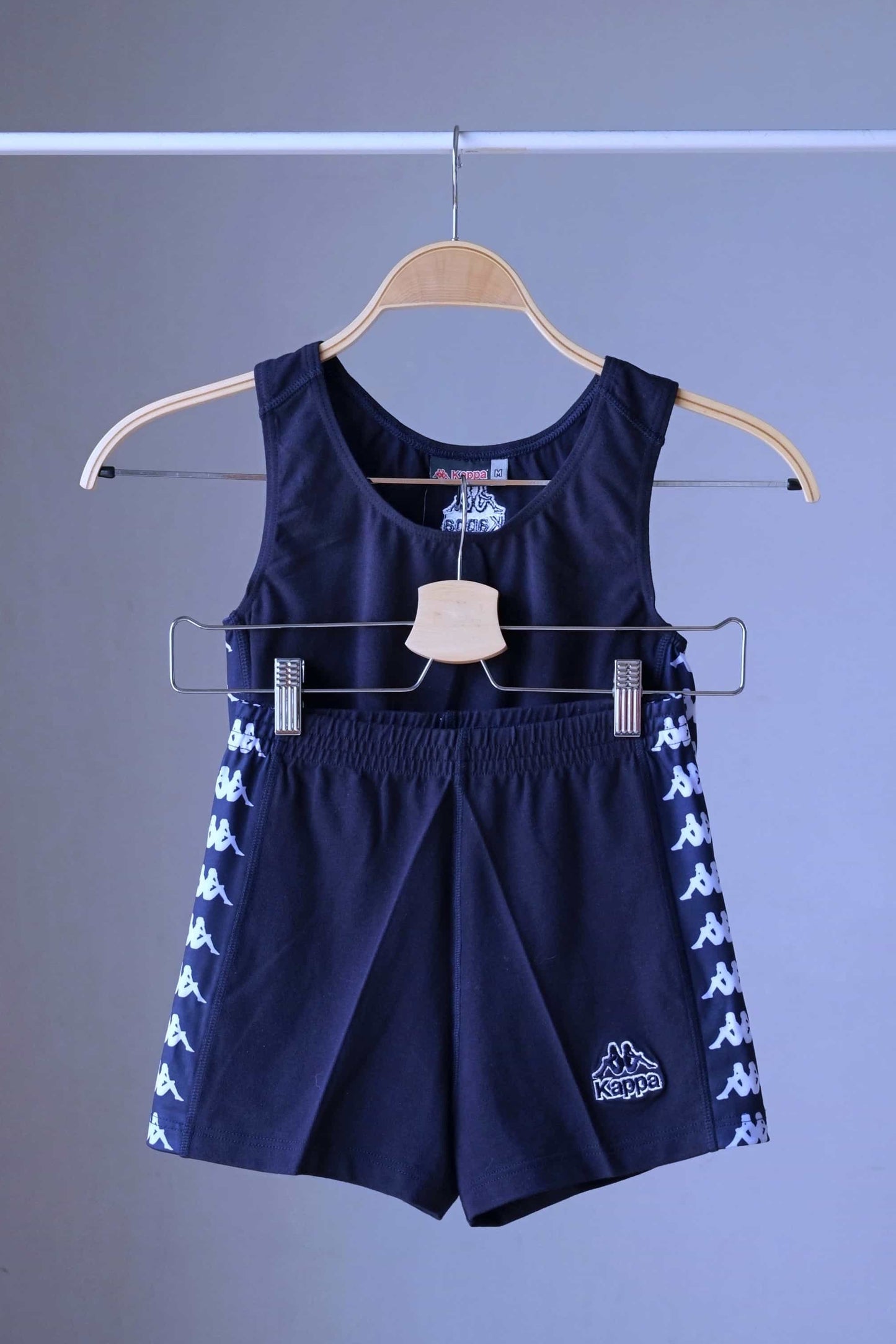Front view of a navy blue KAPPA vintage women's athletic crop top and shorts set on a hanger, with the shorts hanging below the top, displaying the white logo taping on both garments.