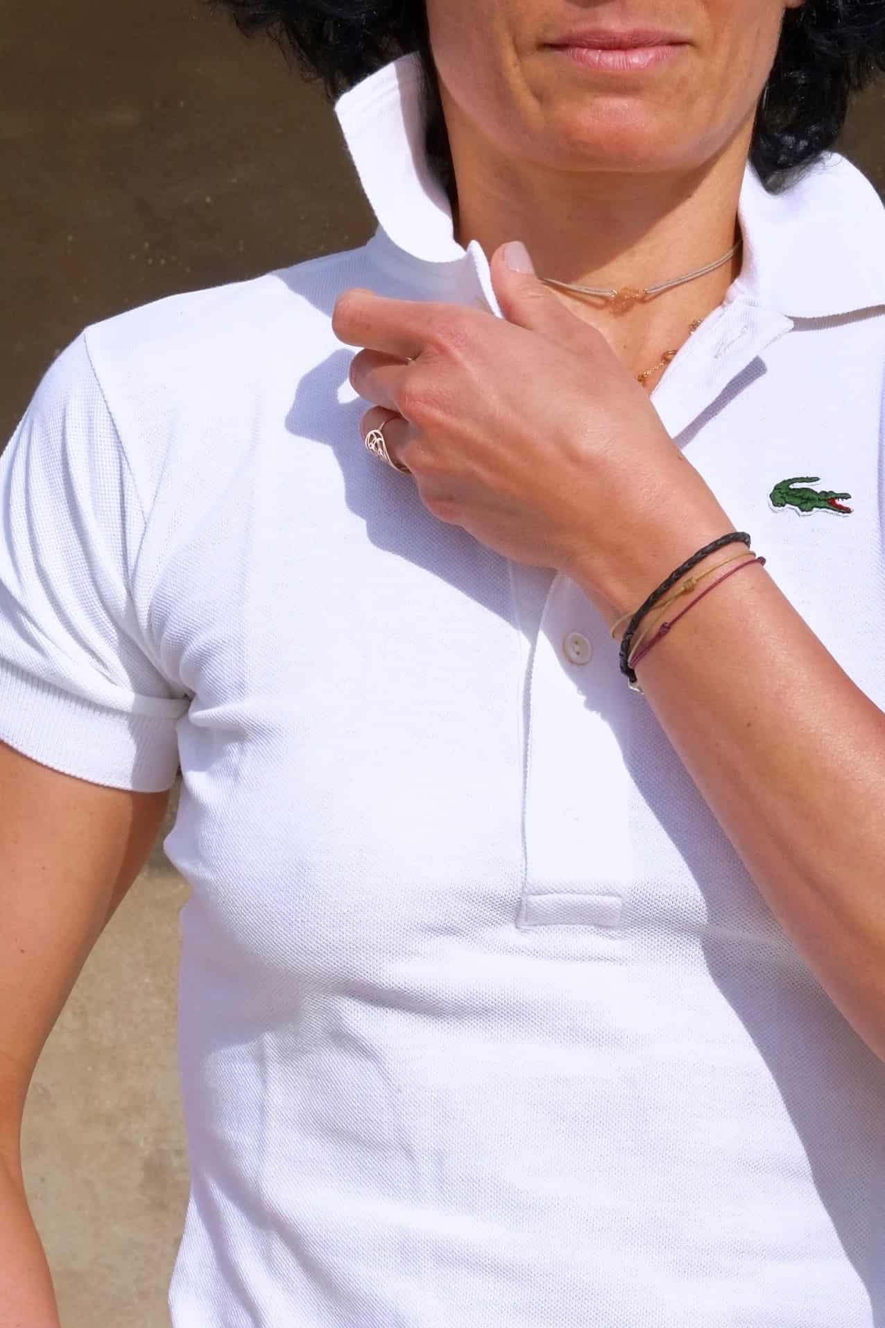 Close shot of Model wearing a white Lacoste polo shirt over denim cut off shorts, standing outside in a sunny spot.