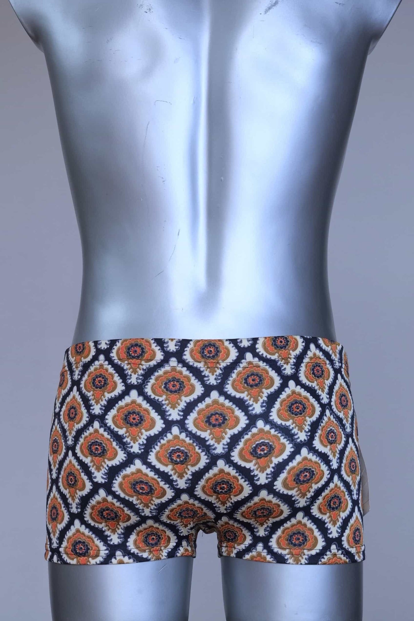 Back view of vintage 60s Lahco swim trunks in navy with an allover brown, orange, and cream geometric medallion print, featuring a zip pocket and original brand tag.
