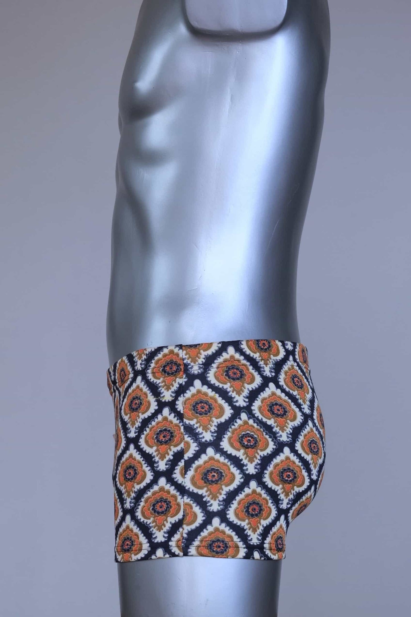 Side view of vintage 60s Lahco swim trunks in navy with an allover brown, orange, and cream geometric medallion print, featuring a zip pocket and original brand tag.