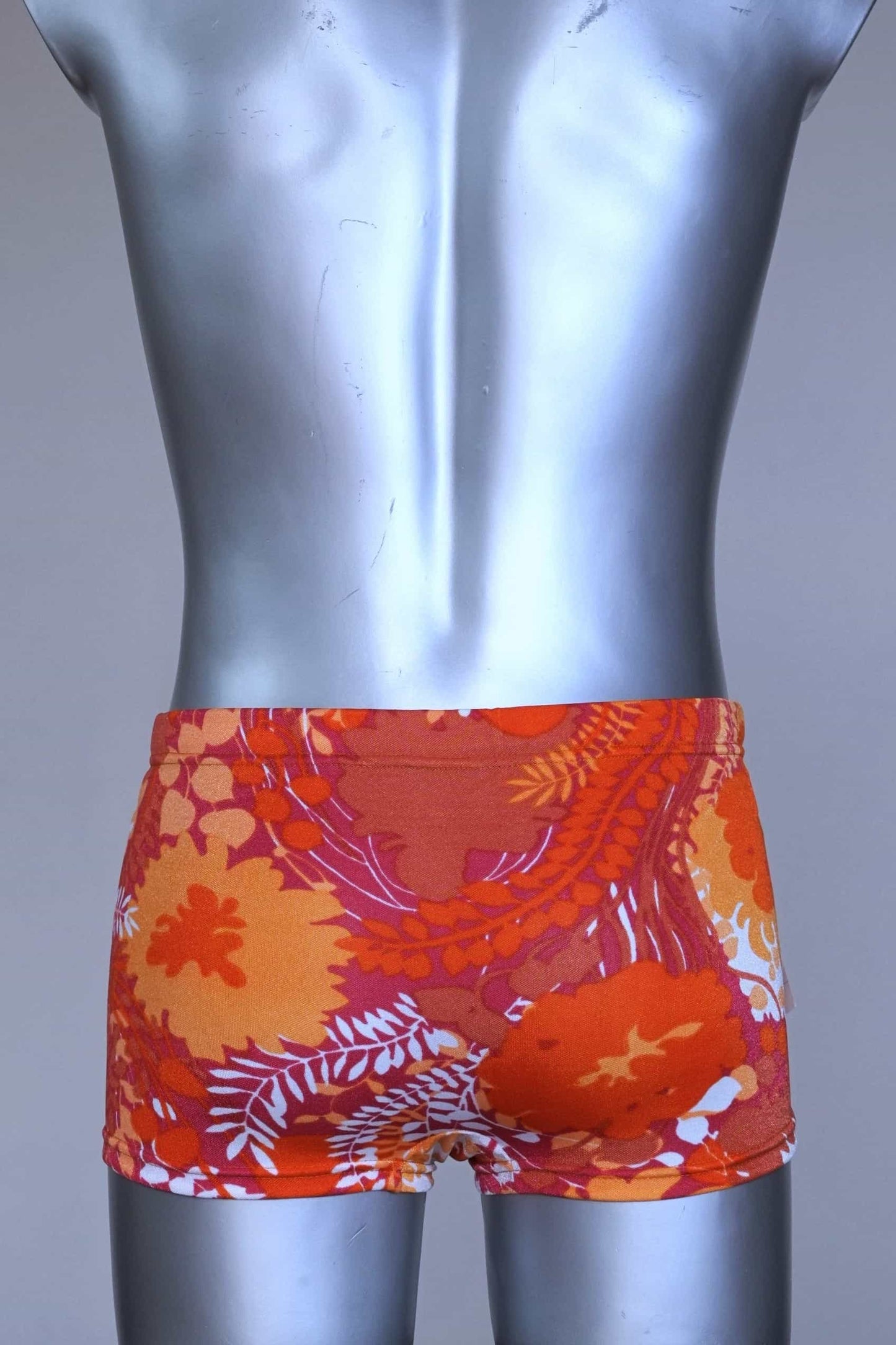 Back view of LAHCO vintage 60s “Rovigo” swim trunks with orange, red, and white floral print, shown on mannequin with original tag.