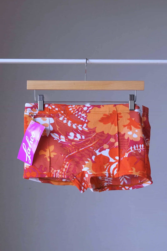 Front view of LAHCO vintage 60s “Rovigo” swim trunks with orange, red, and white floral print, shown on a wooden hanger with original tag.