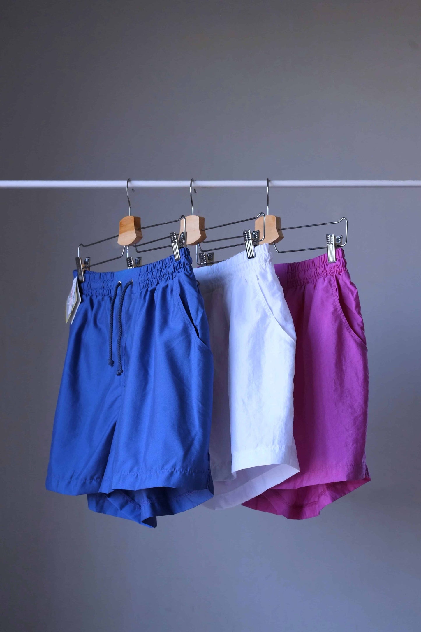 Three pairs of vintage Löffler shorts in blue, white, and magenta hanging together on a clothing rack.