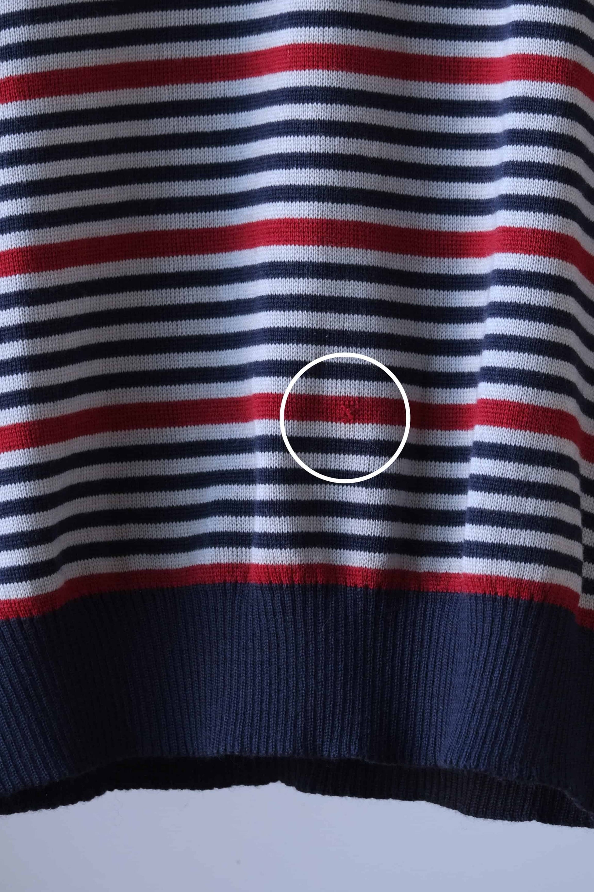 Close-up of a vintage Löffler striped V-neck sweater, highlighting a hole on the front. The sweater features horizontal stripes in burgundy, navy blue, grey, with a ribbed hem and cuffs. A white circle marks the repaired area for visibility.