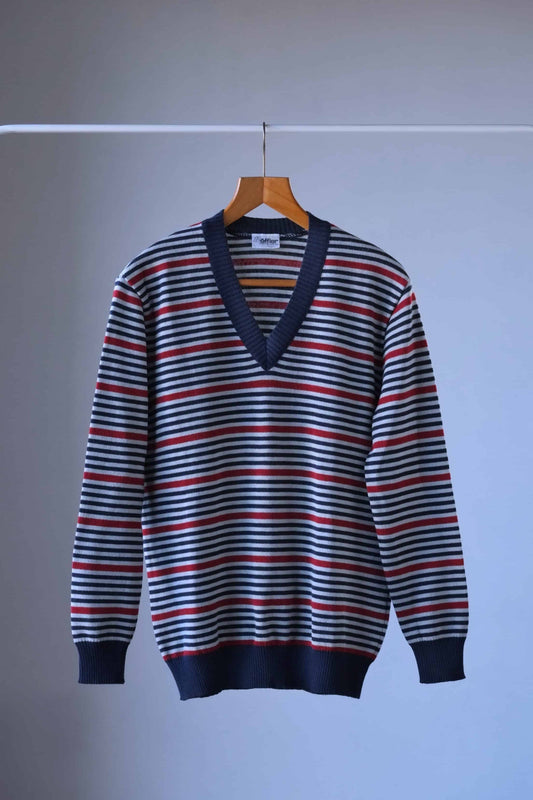 Loffler vintage sweater with horizontal stripes in shades of blue, red, and grey. It has a v-neck and is hanging on a wooden hanger.
