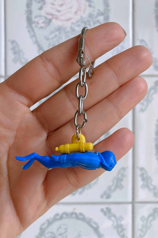 Close view of a hand holding a blue and yellow Nemrod diver figurine keychain.