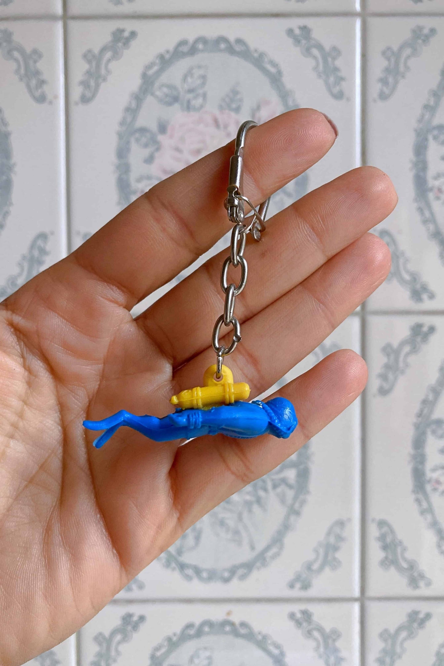A hand holding a blue and yellow Nemrod diver figurine keychain.