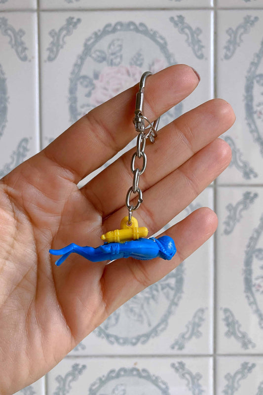 A hand holding a blue and yellow Nemrod diver figurine keychain.