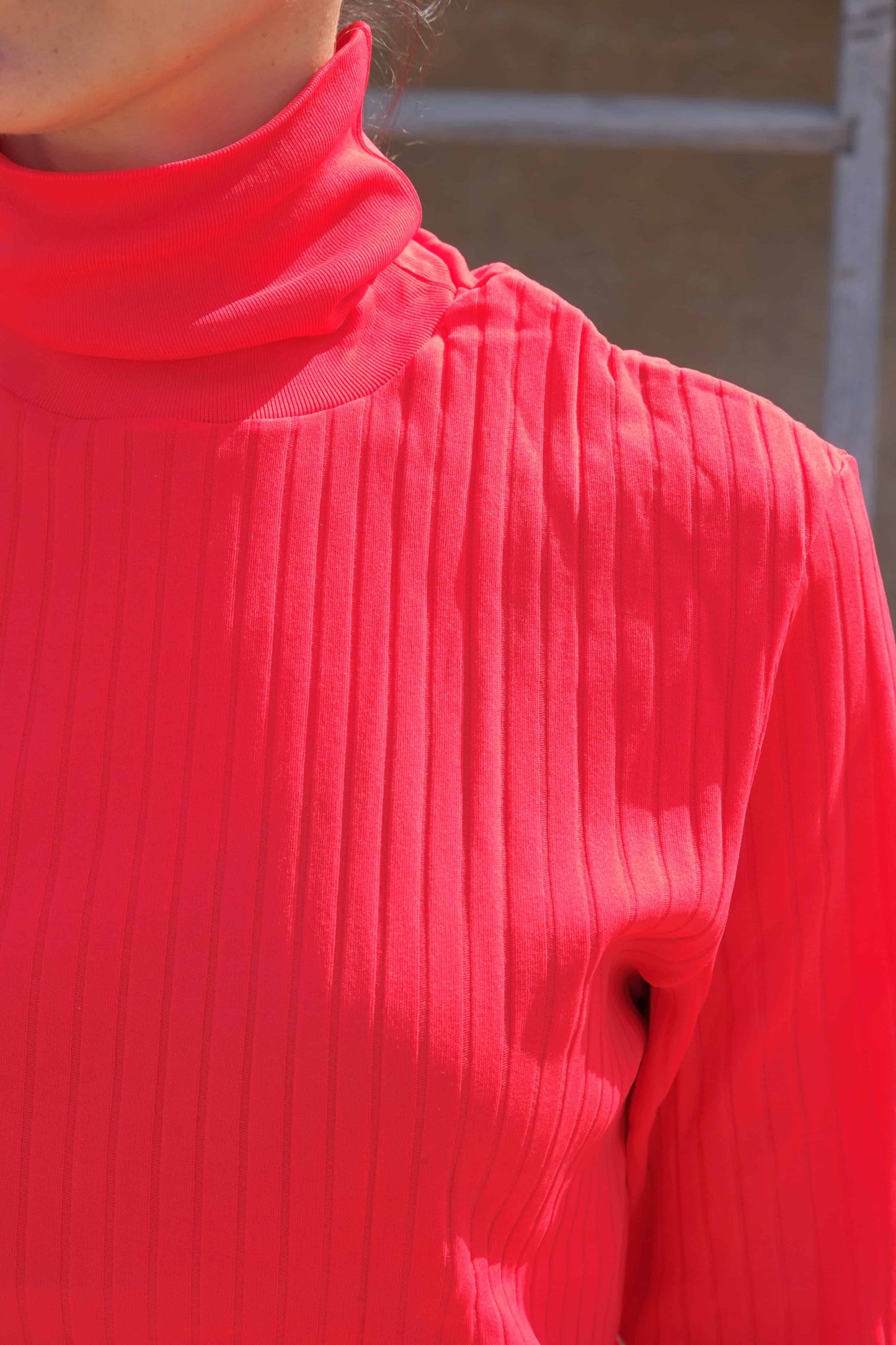 Detail shot of a vibrant red ribbed turtleneck top showcasing the texture and knit pattern.