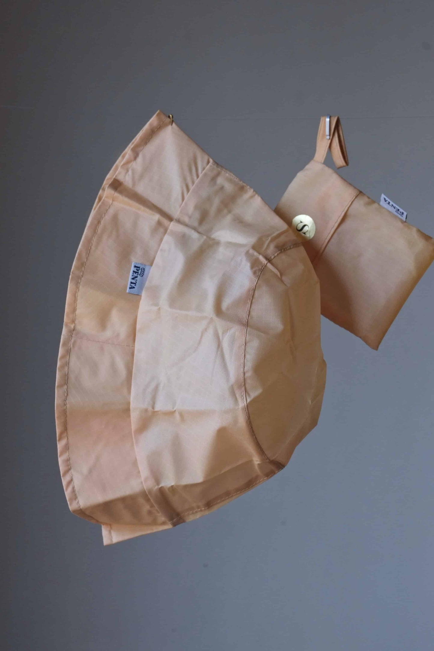 Beige rainproof bucket hat with its pouch hanging in front of a grey background