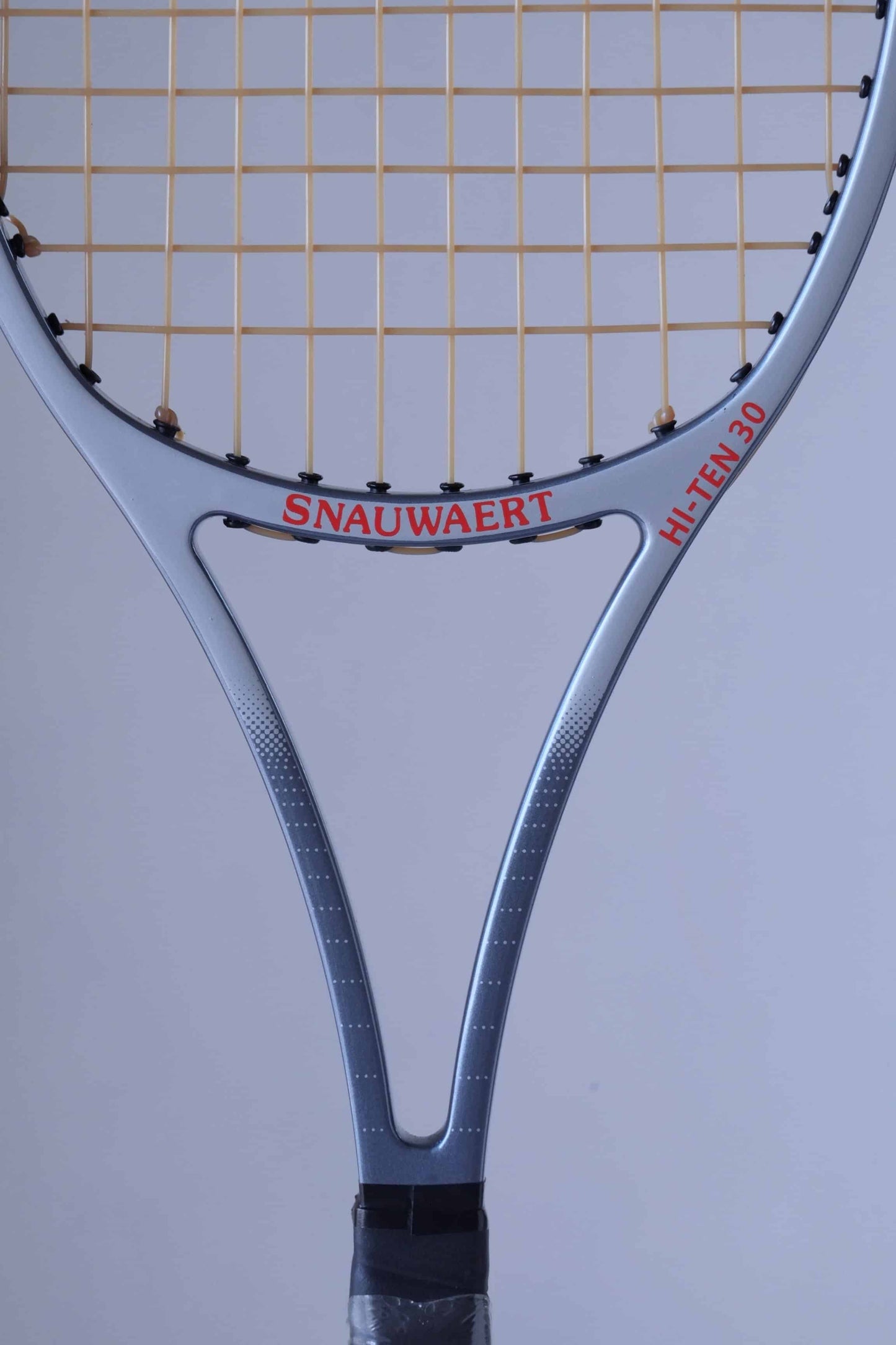 Close-up of the throat area of a Snauwaert Hi-Ten 30 tennis racket, highlighting the red Snauwaert logo and model name in bold lettering on the grey frame.