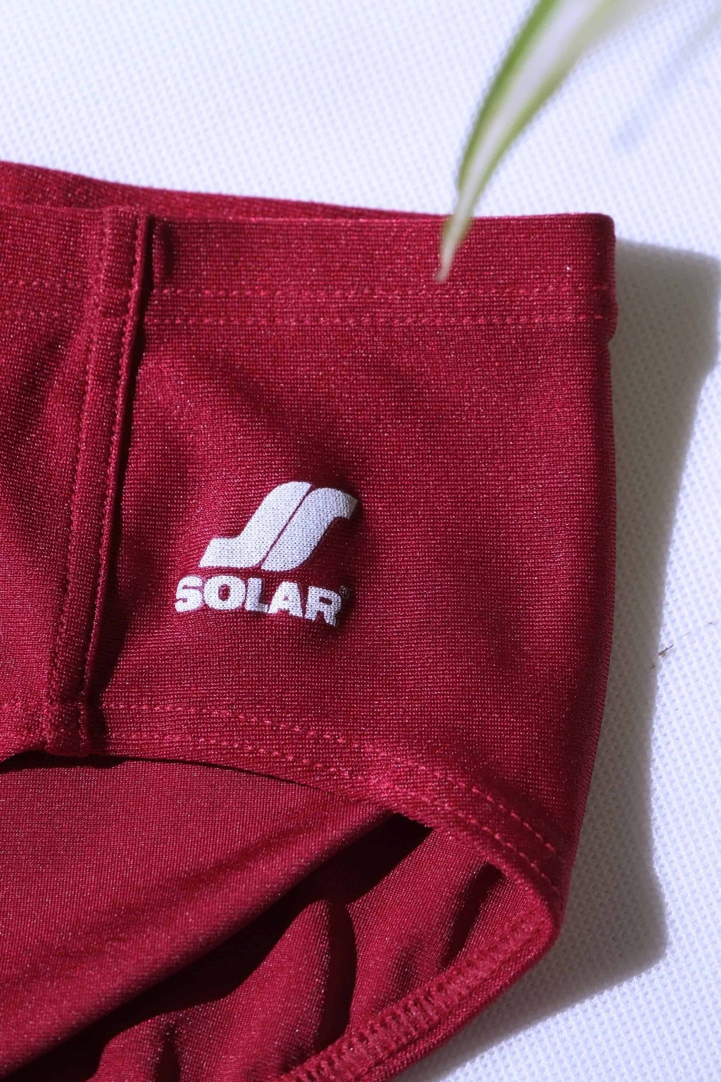 Close-up of a pair of vintage burgundy swim briefs with a Solar logo on a white background