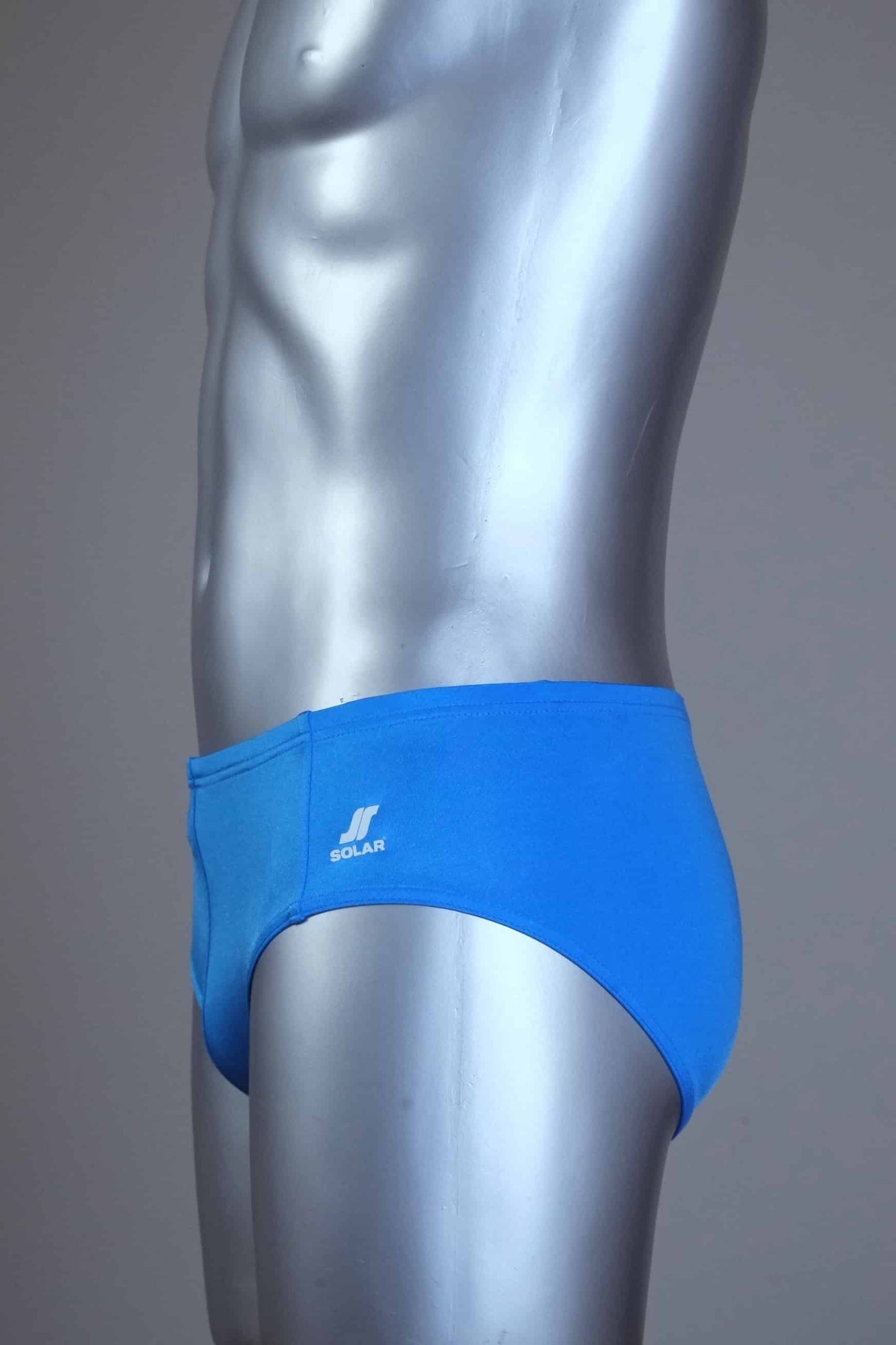 Side view of a mannequin wearing a pair of vintage 70s blue swim briefs with a visible brand logo on a gray background
